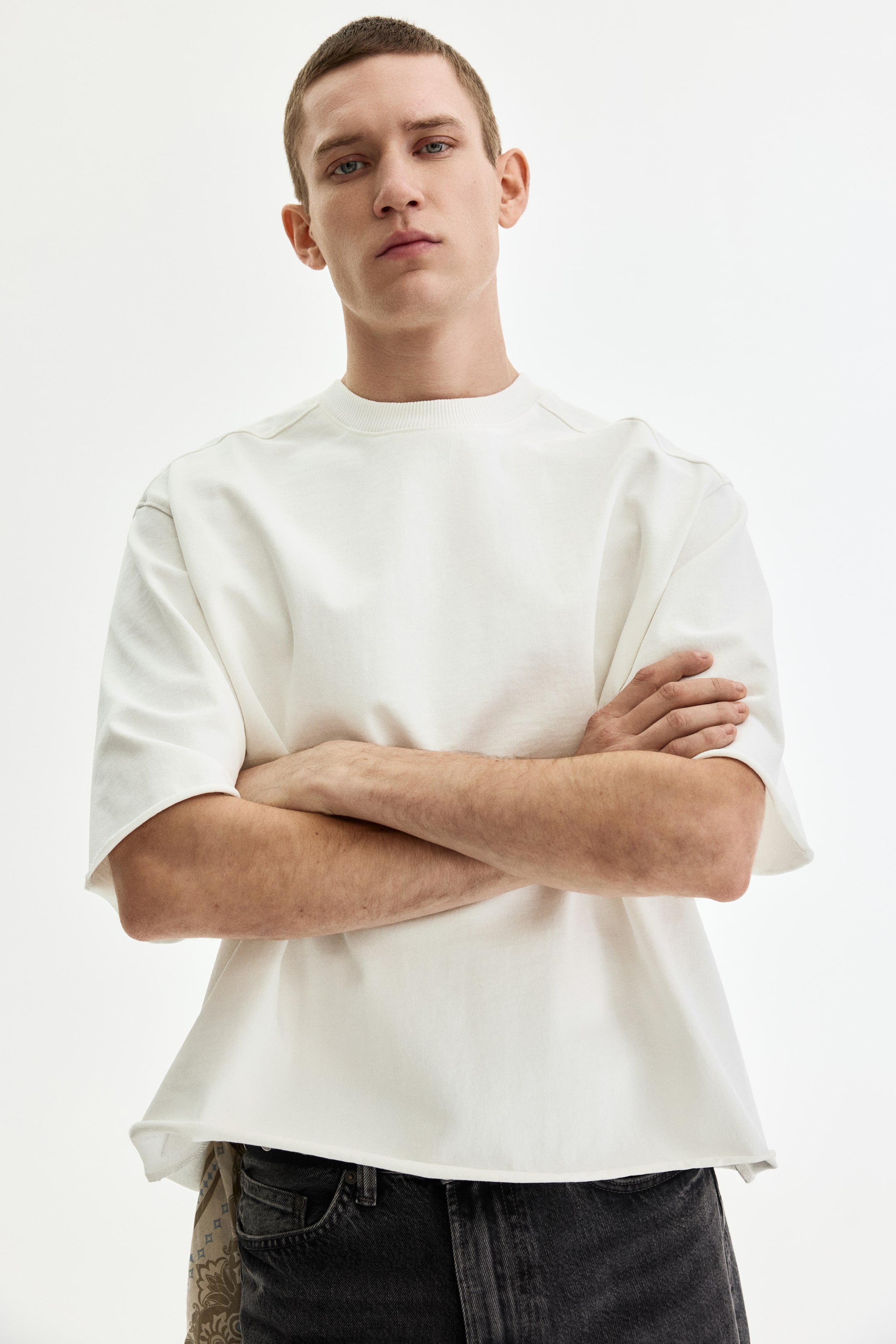 View larger image: Model wears an oversized white T-shirt with a ribbed crewneck collar, dropped shoulders, loose short sleeves, and an unfinished, curved bottom hem.