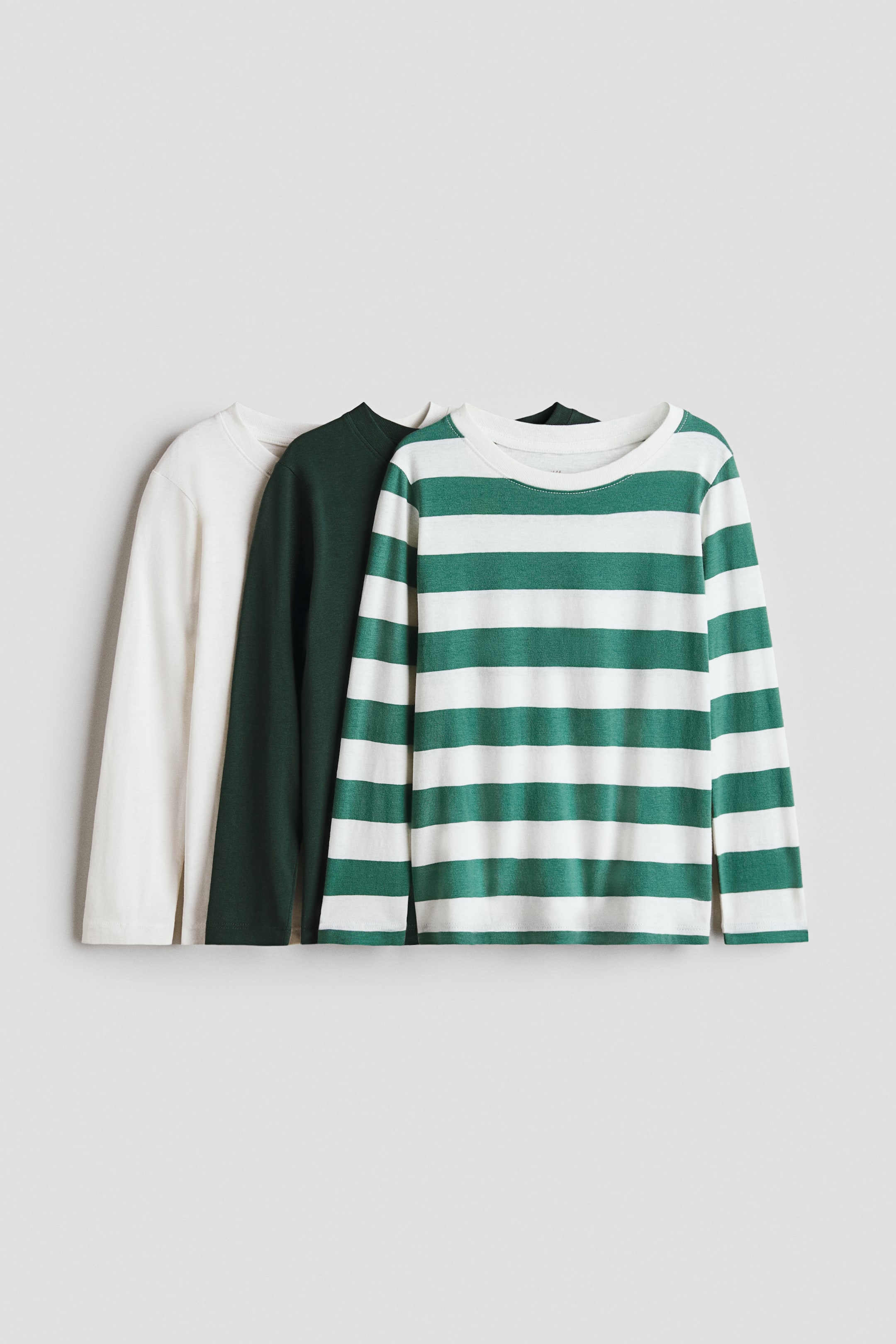 Grotere afbeelding bekijken: Drie tops met lange mouwen van zachte katoenen jersey worden van voren getoond, elk met een ronde hals en een smalle afwerking. Eén top is gebroken wit, een andere is donkergroen en de derde heeft groen-witte strepen.