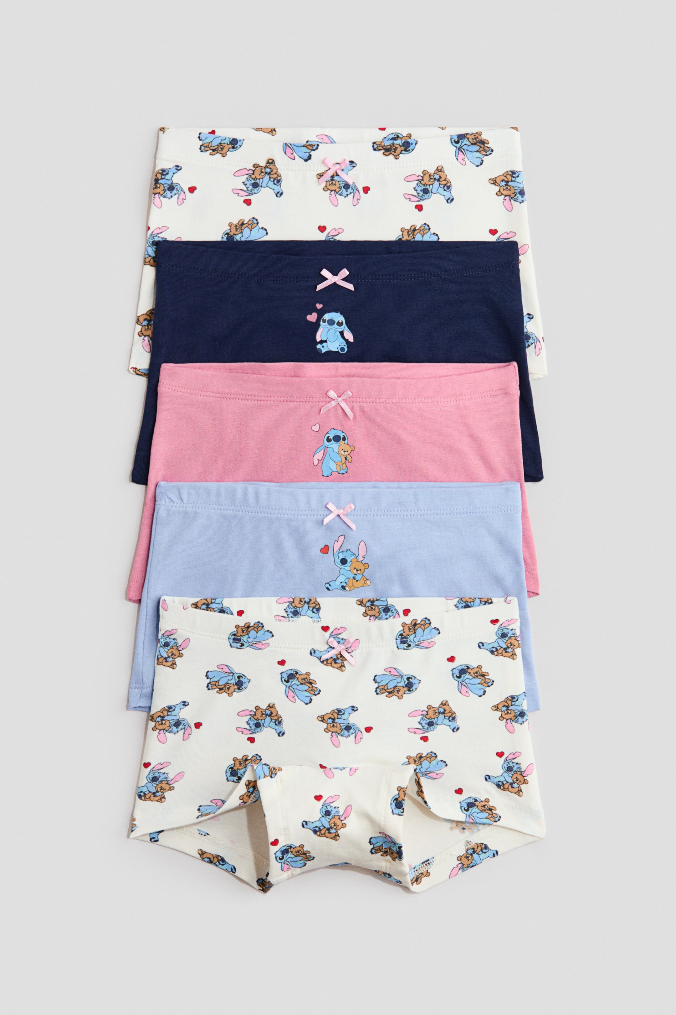 View larger image: A set of five boxer briefs in soft cotton jersey is stacked, showcasing their front view. Two pairs are solid navy blue and pink, each featuring an embroidered Stitch character and a small pink bow at the elasticated waist, while the remaining three pairs are white, light blue, and cream, all displaying an all-over print of Stitch and teddy bears, accented with a small pink bow at the elasticated waist.