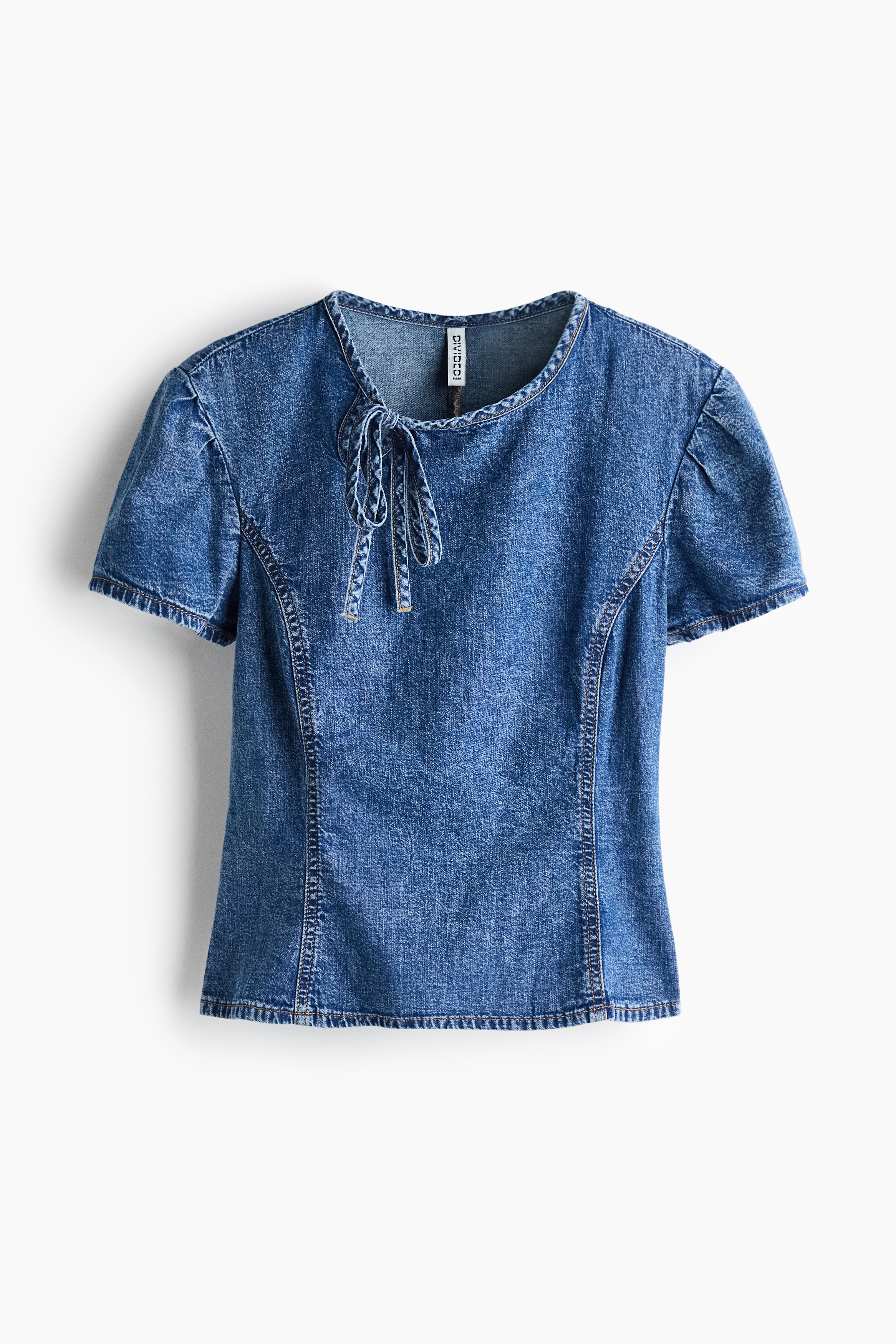 NgÆ°á»i máº«u Äang máº·c má»t chiáº¿c Ã¡o blouse denim Ã´m dÃ¡ng, dÃ¡ng ngáº¯n. Ão cÃ³ cá» trÃ²n vá»i chi tiáº¿t khoÃ©t giá»t lá» vÃ  dÃ¢y buá»c máº£nh á» má»t bÃªn, tay Ã¡o phá»ng ngáº¯n, cÃ¹ng cÃ¡c ÄÆ°á»ng may princess ná»i cháº¡y dá»c phÃ­a trÆ°á»c.
