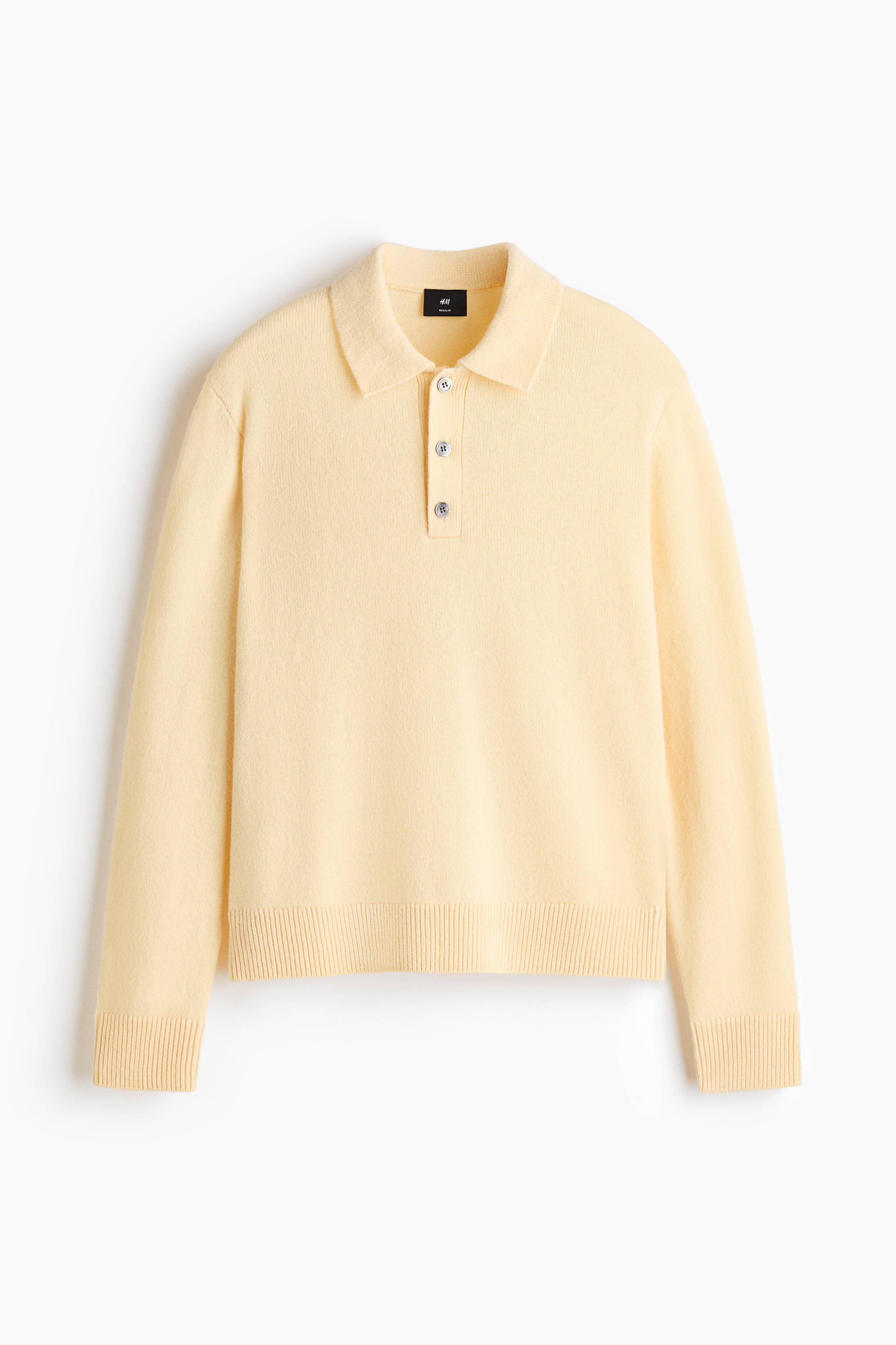 A pale yellow, fine-knit polo shirt is shown in a front view, featuring a classic polo collar, a three-button placket, and long sleeves. The garment displays a regular-fit silhouette with ribbed detailing at the cuffs and hem.