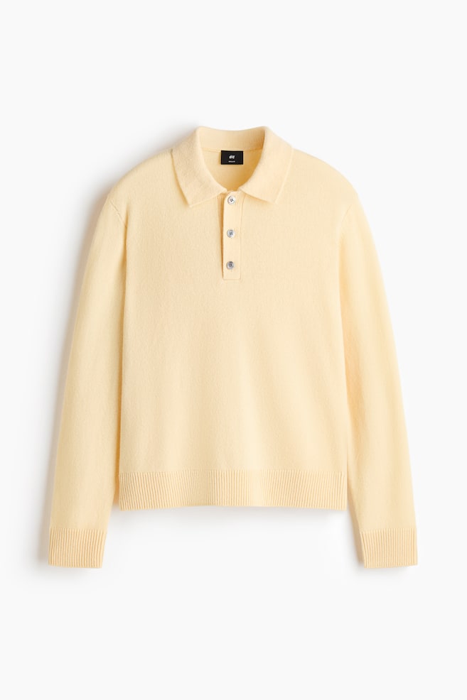 A pale yellow, fine-knit polo shirt is shown in a front view, featuring a classic polo collar, a three-button placket, and long sleeves. The garment displays a regular-fit silhouette with ribbed detailing at the cuffs and hem. - 1
