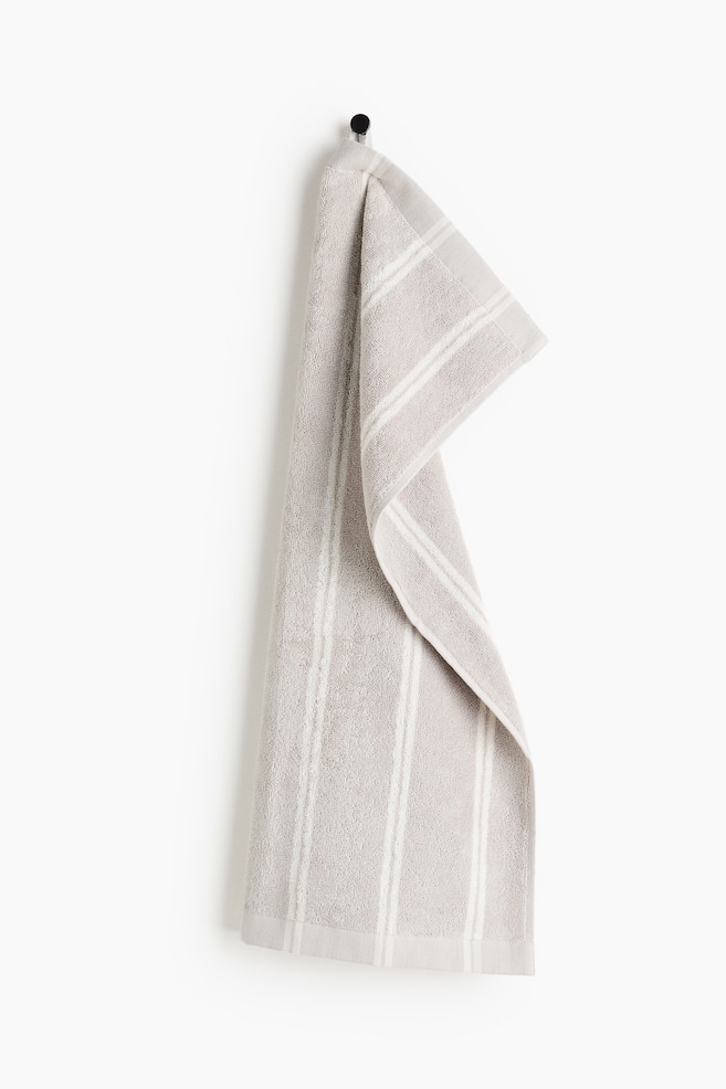 A light grey terry cloth towel with multiple white vertical stripes is hanging from a black hook, presenting a front view with a fold draping to the right. - 1