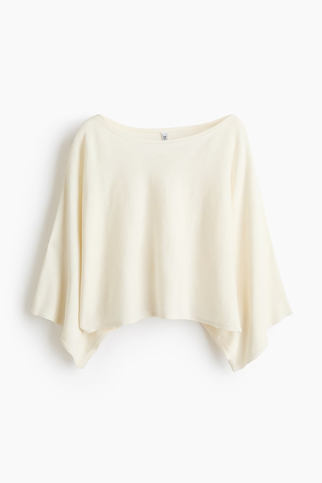 Ein cremefarbenes Poncho-Top mit einem Bootsausschnitt und weiten Dolman-Ärmeln. Die Vorderseite präsentiert einen asymmetrischen Saum, der einen entspannten Fall erzeugt. - 1