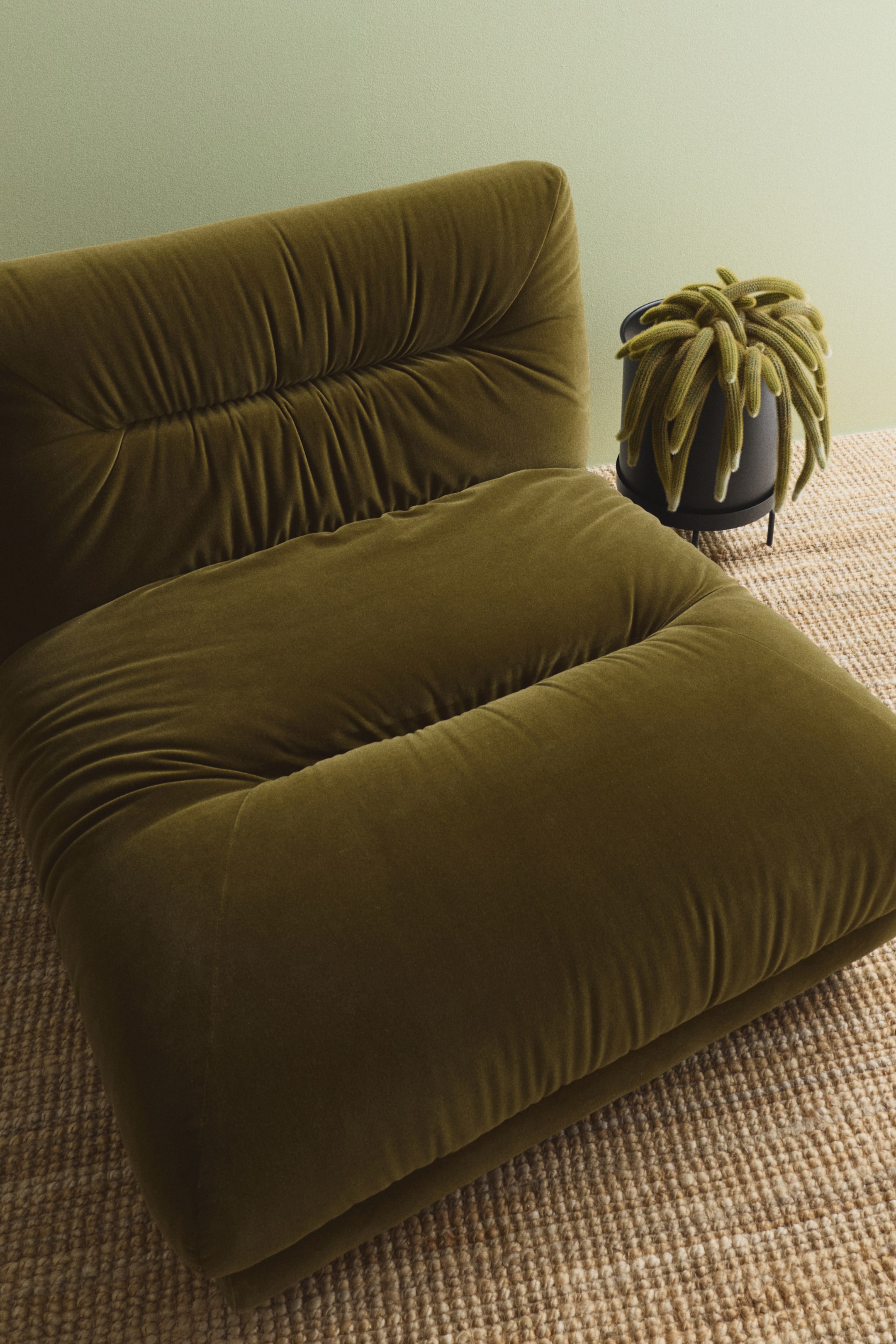 Größeres Bild anzeigen: Ein großer, dunkler Metallpflanzentopf sitzt in einem passenden dreibeinigen Pflanzenständer, aus einer frontseitigen Perspektive betrachtet. Eine hellgrüne, rankende Sukkulente füllt den Topf aus und quillt über den Rand hinaus.