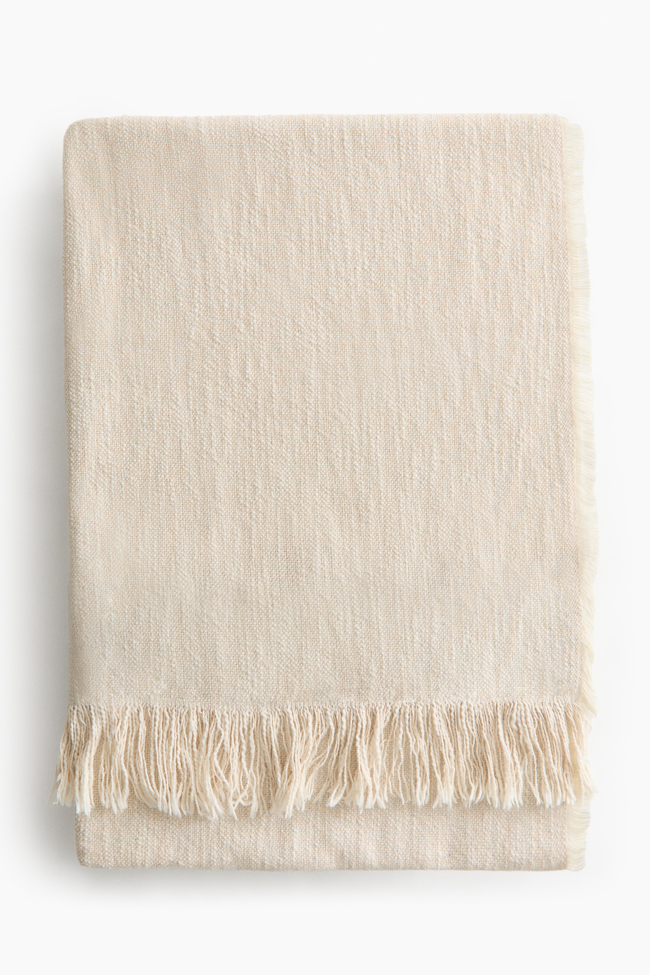 View larger image: A cream-coloured blanket is folded neatly, displaying a textured woven surface and fringe detailing along its lower edge.