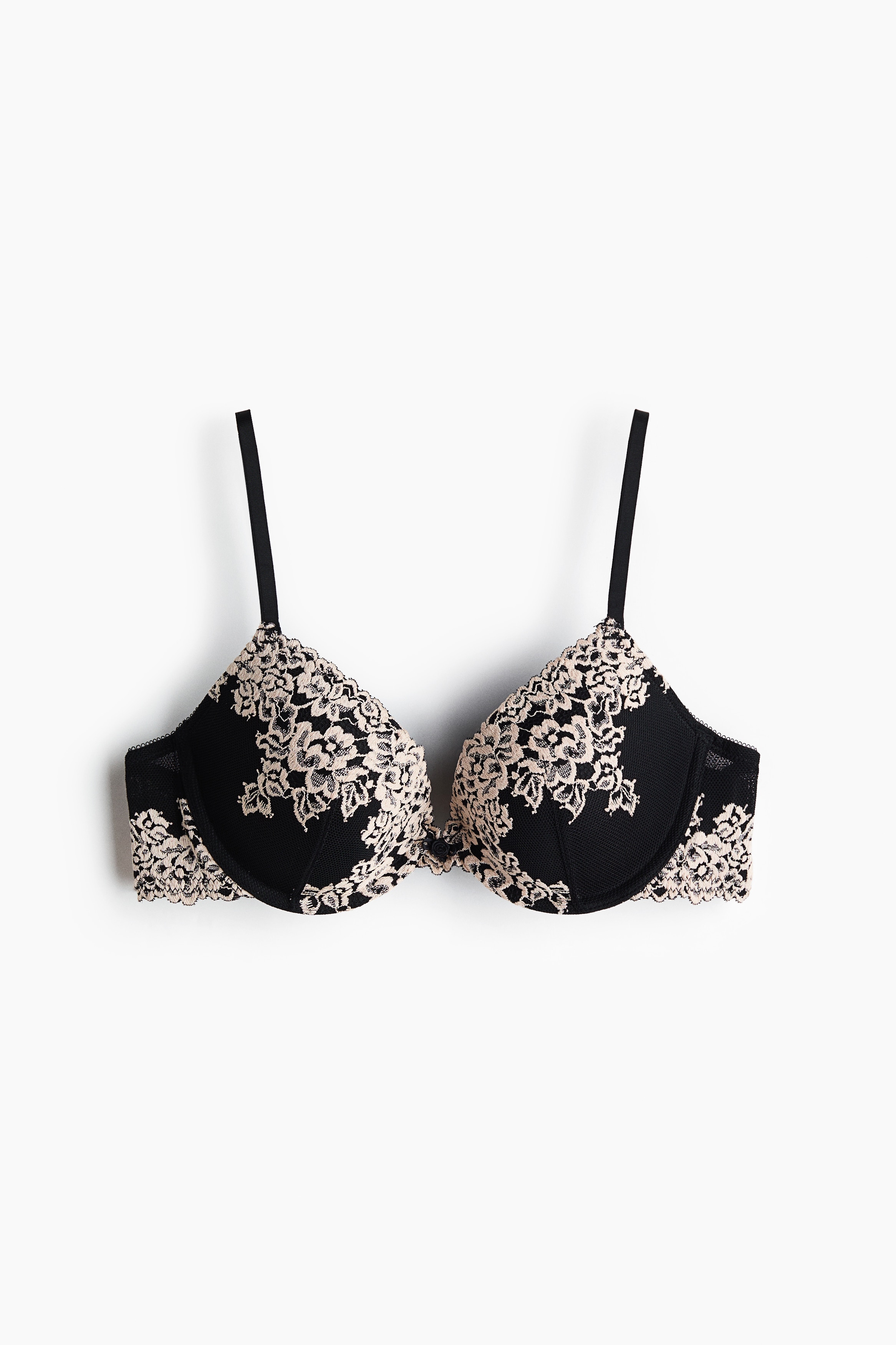 Una modella indossa un reggiseno push-up nero con coppe imbottite e con ferretto, decorate da un rivestimento in pizzo floreale bianco. Il reggiseno Ã¨ abbinato a slip coordinati neri in pizzo e mesh.