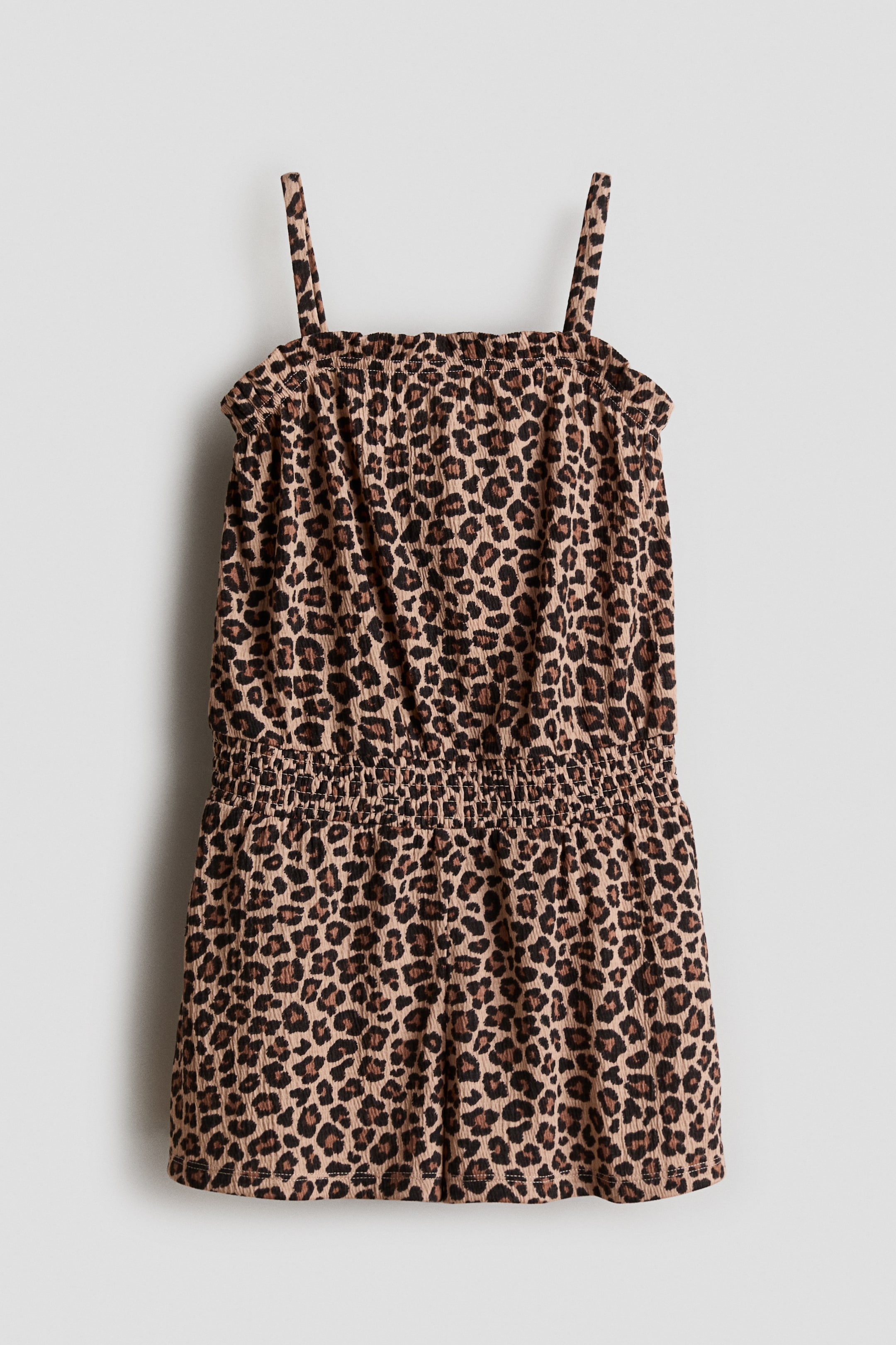 View larger image: The jumpsuit showcases a leopard print pattern on a soft weave, prominently displayed at the front. It features a straight neckline with smocked elastication and a frill trim around the top. The design includes narrow shoulder straps and smocked elastication at the waist, offering both style and comfort.