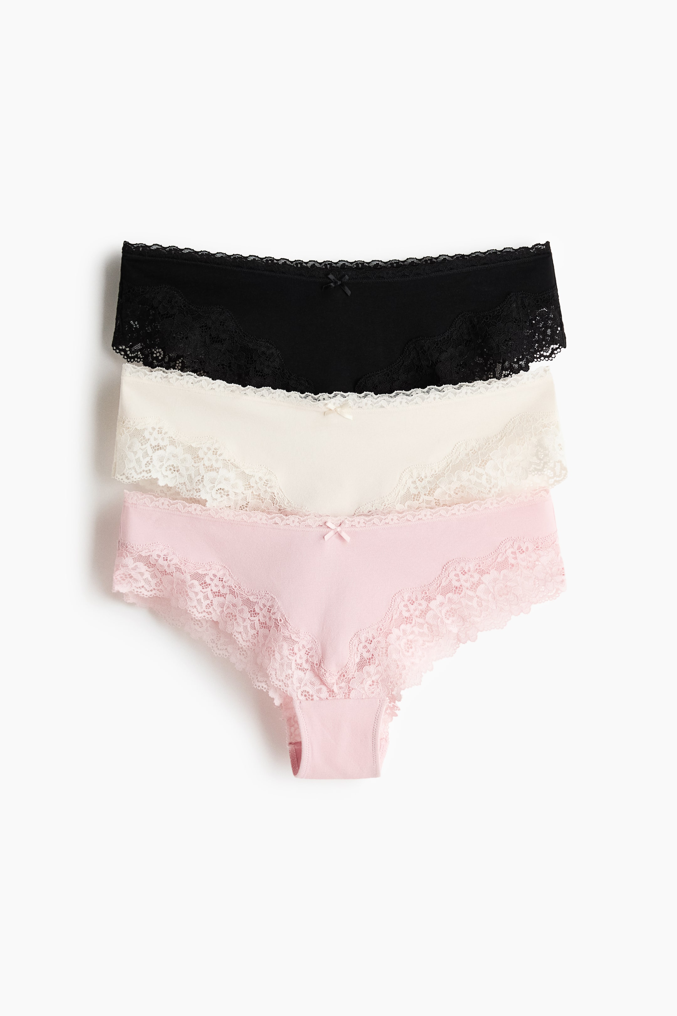 Ver imagen más grande: Tres bragas están mostrando sus lados FRONTALES, apiladas con una braga negra arriba, una braga crema en el medio y una braga rosa claro en la parte inferior. Cada braga presenta un cuerpo de jersey de algodón con bordes de encaje a lo largo de la cintura media y las aberturas de las piernas, y un pequeño lazo adorna el centro frontal.