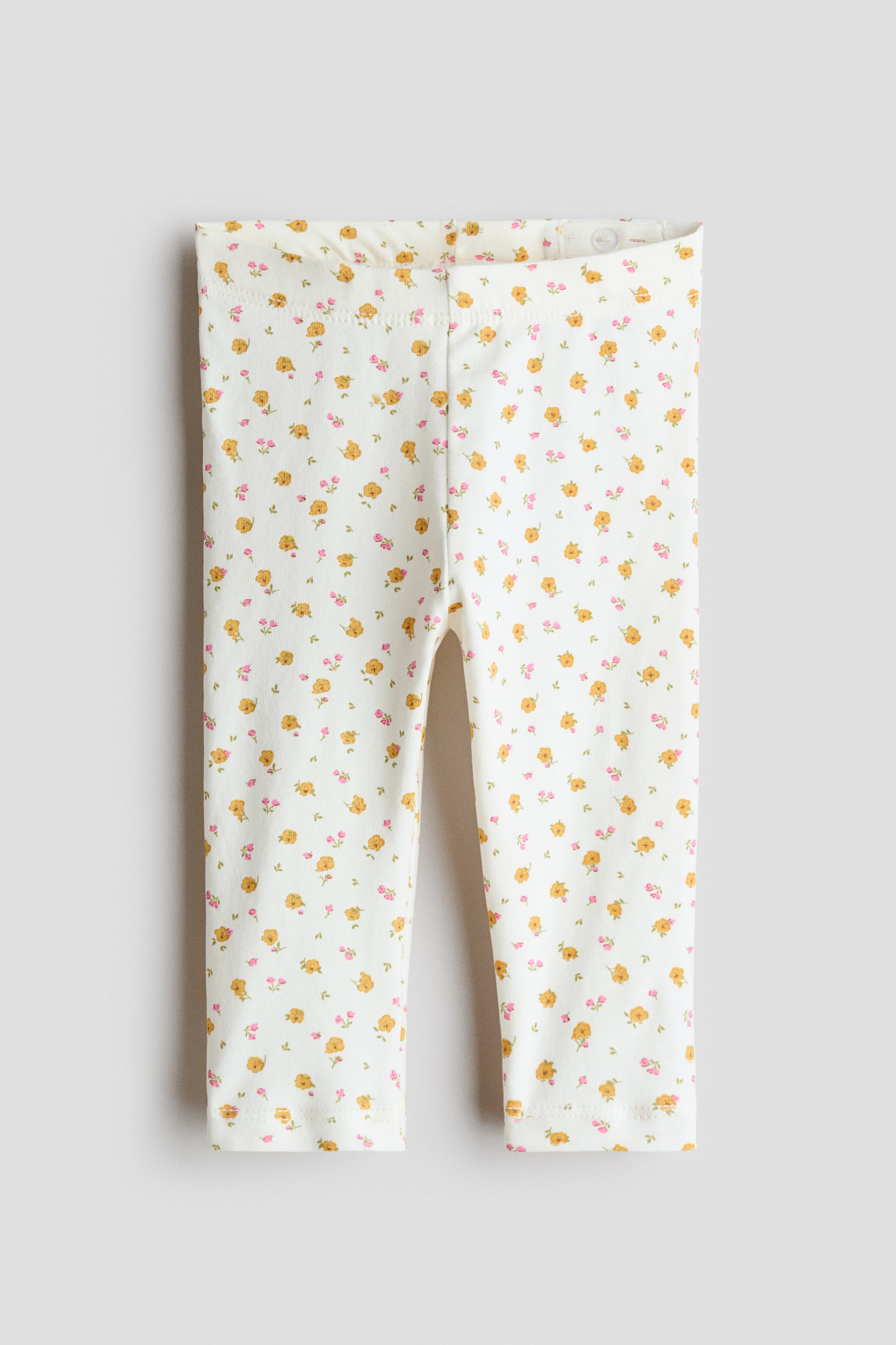 Ver imagen más grande: Los leggings se presentan de frente, confeccionados en un tejido de jersey de algodón crema con un estampado completo de pequeñas flores amarillas y rosas. Están diseñados con una cintura elástica ajustable.