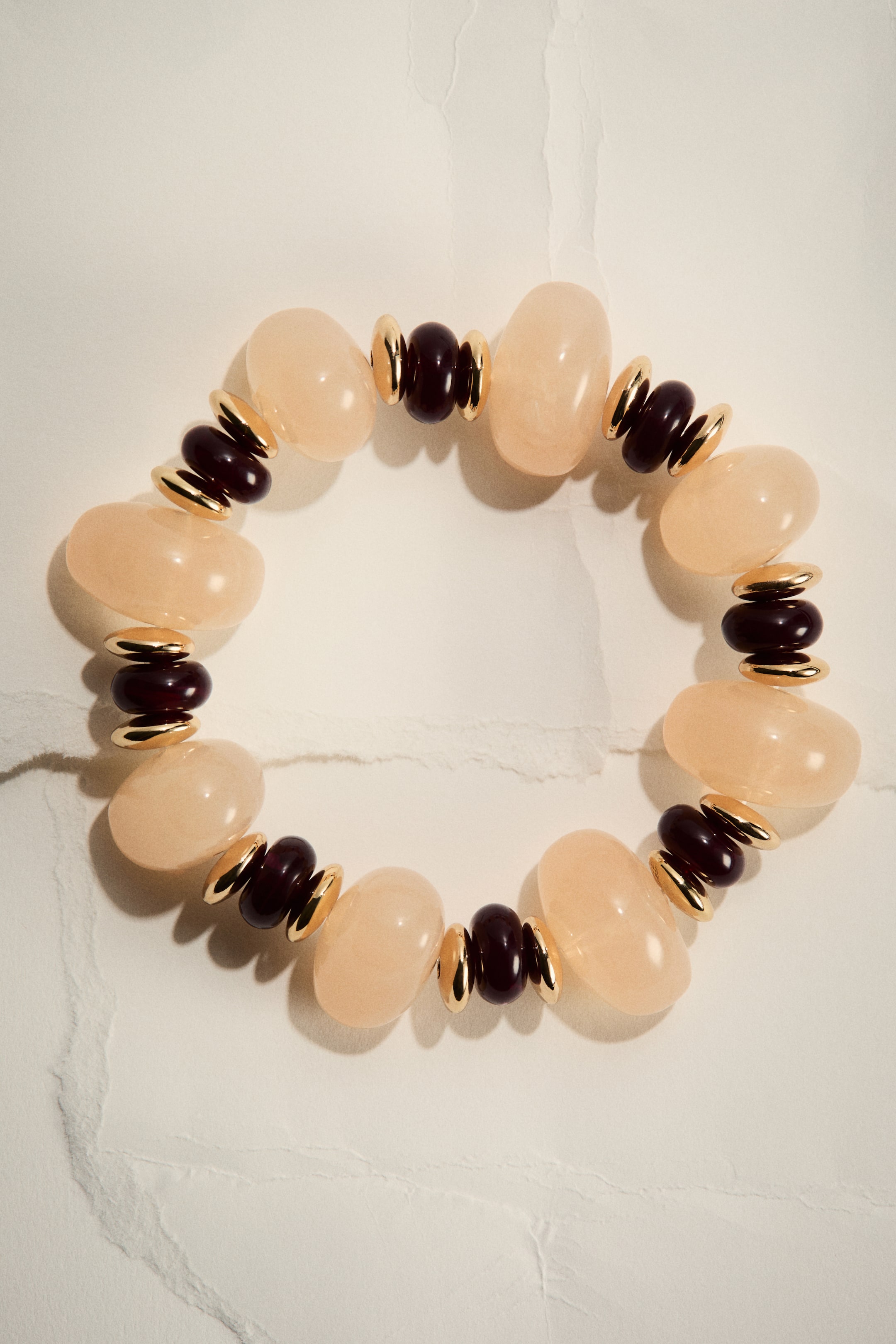 View larger image: An elasticated bracelet is presented from the front, showcasing alternating light peach, irregularly shaped beads and smaller, dark reddish-brown barrel beads, which are separated by gold-toned disc spacers.