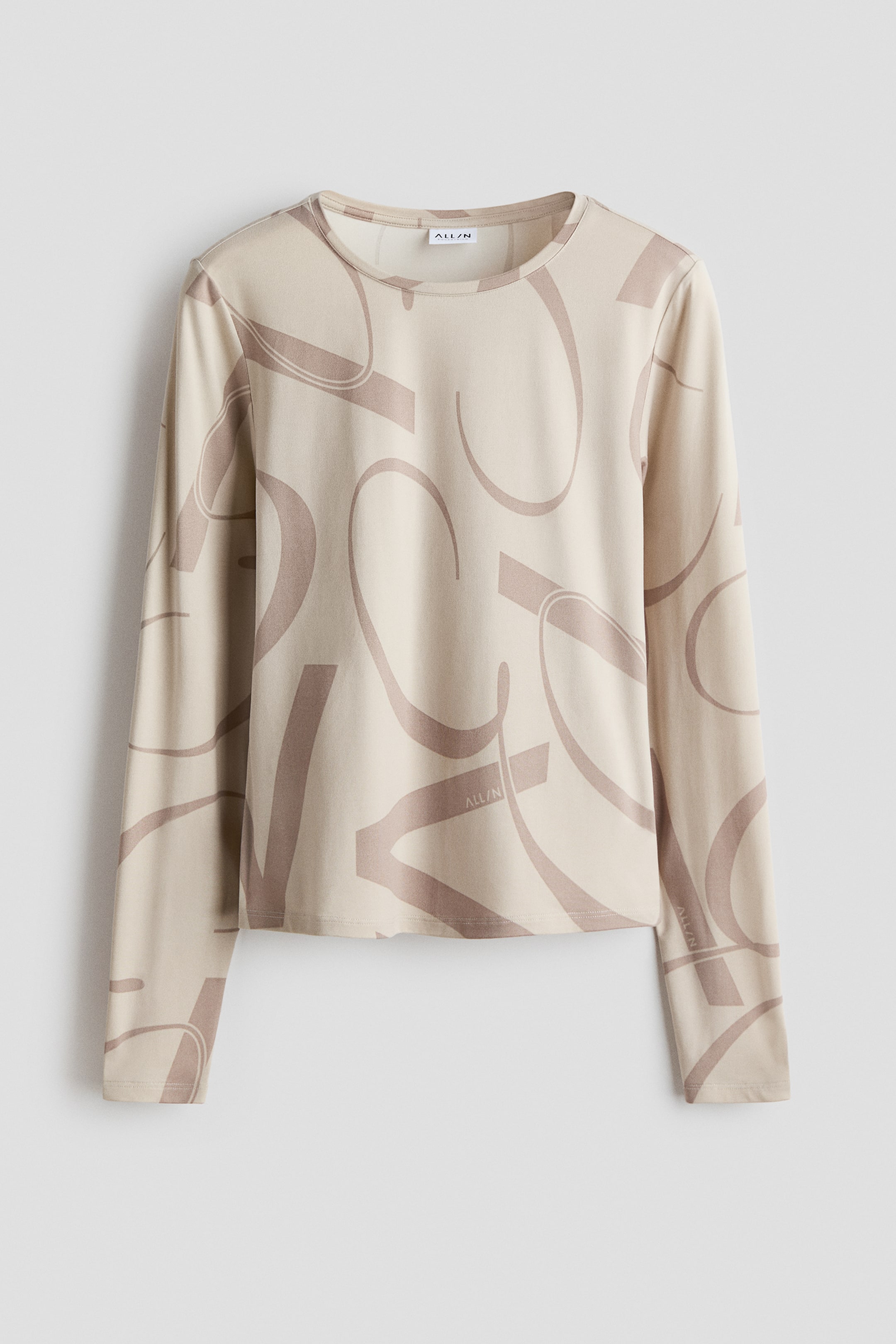 Größeres Bild ansehen: Ein langärmliges Oberteil zeigt eine hellbeige Farbe mit einem allover-stilisierten „ALL/N“-Grafikprint in dunklerem Tan. Es verfügt über einen Rundhalsausschnitt und lange Ärmel und ist in Vorderansicht abgebildet.