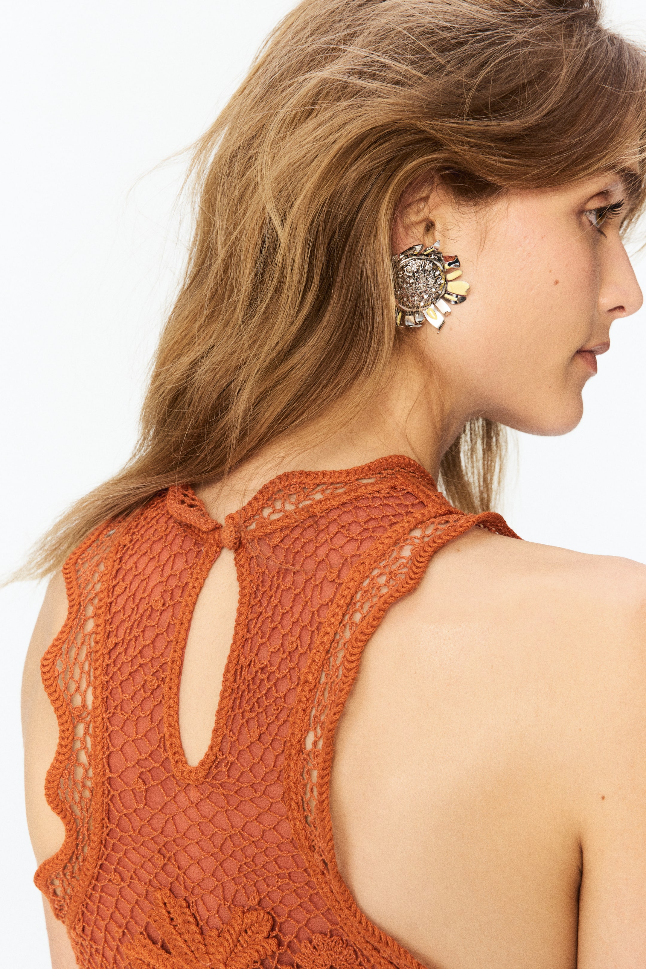 View larger image: An earring featuring a textured, ornate central disc encircled by radiating, metallic petal-like elements in silver and gold tones, positioned on the ear.