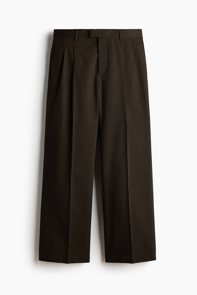Dark-colored trousers are presenting from the front, featuring an extended waistband with belt loops and a concealed fly closure. They are showcasing a loose fit with subtle side pockets and visible creases running down the front of each leg. - 1