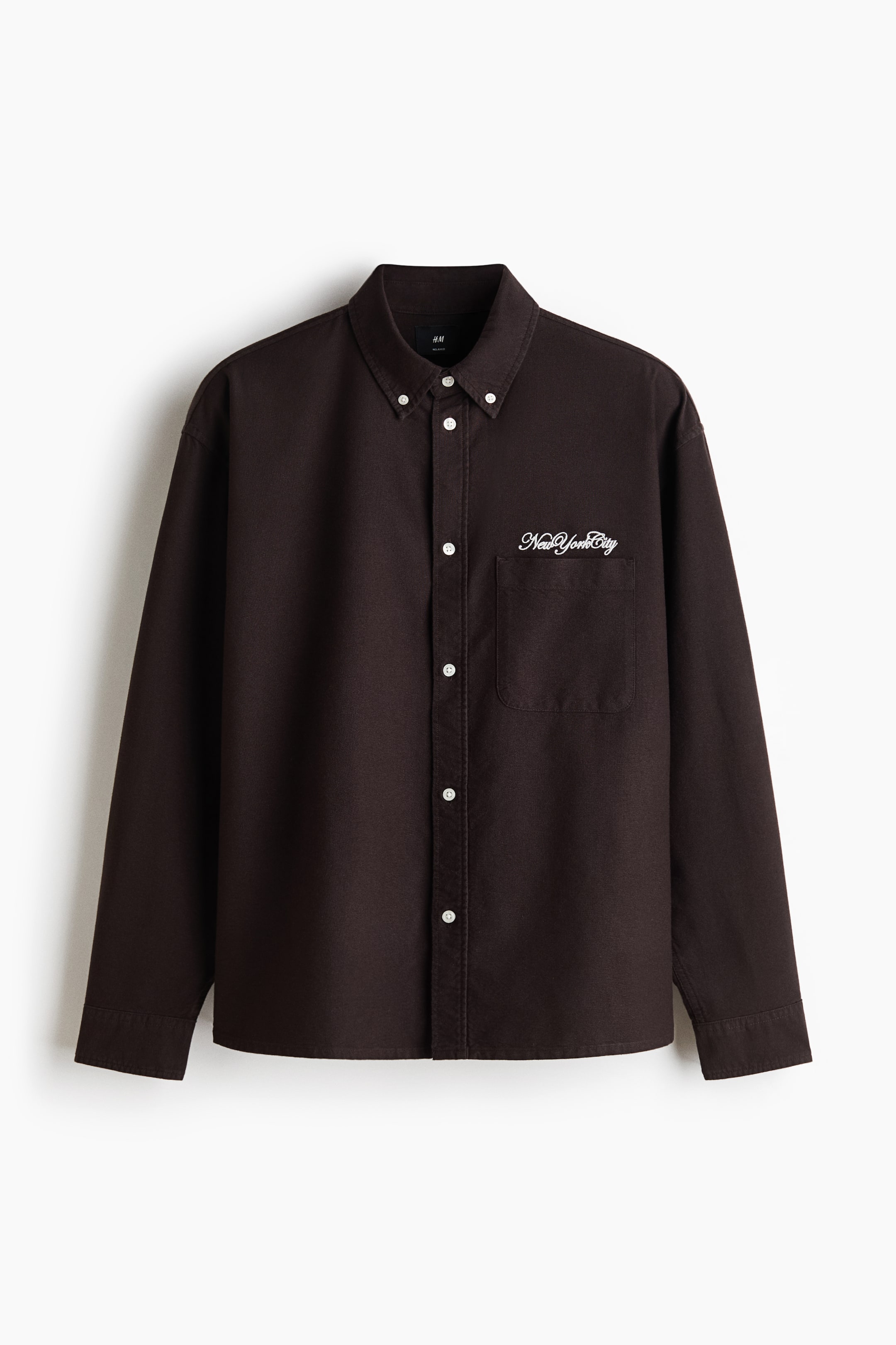 View larger image: A dark brown shirt features a button-down collar and a full front placket with white buttons. It comes with long sleeves, single-button cuffs, and a patch pocket on the left chest, detailed with white script embroidery reading 'New York City'.