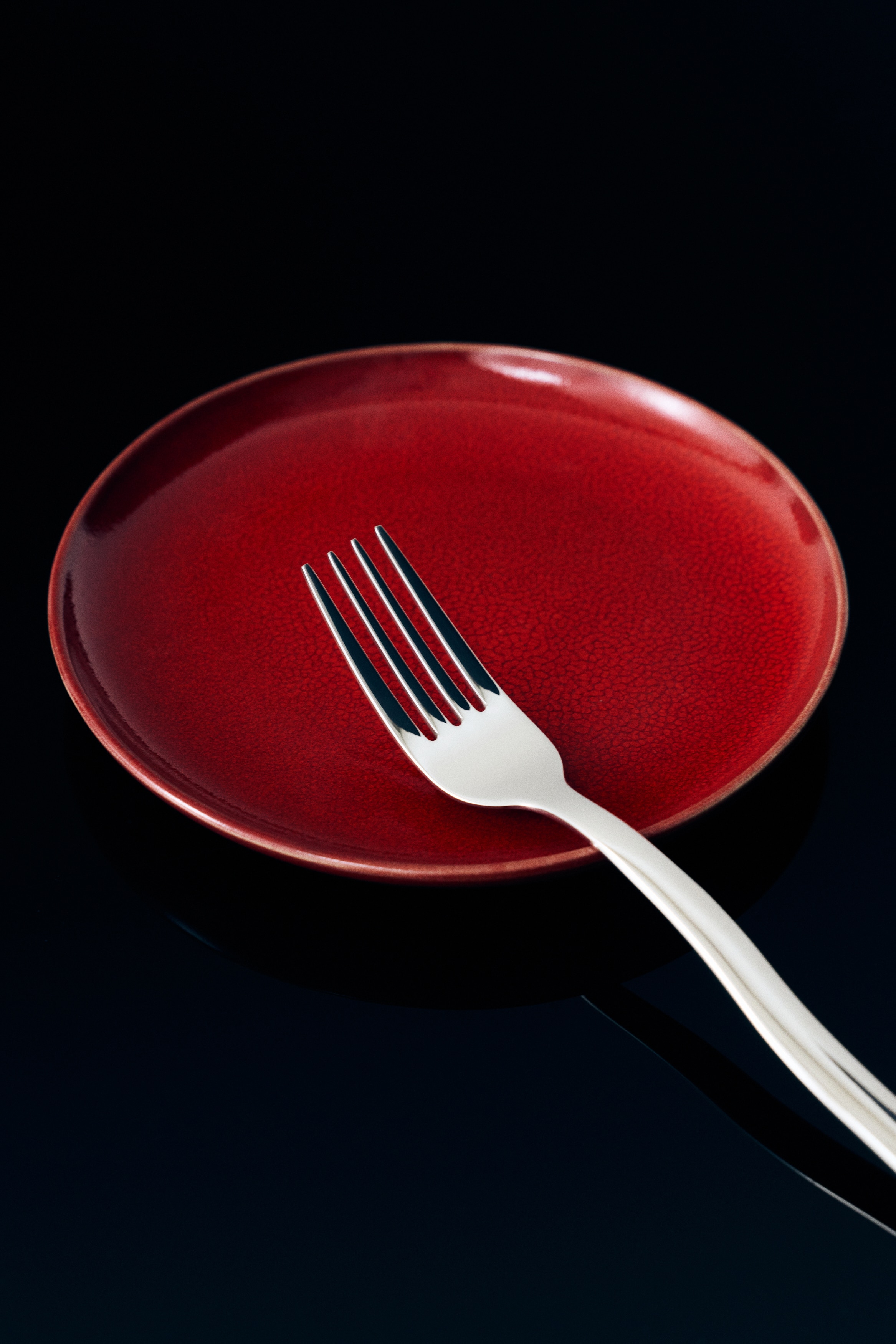 Un plato cerámico redondo muestra un esmalte rojo vibrante y brillante con un fino patrón craquelado, visto desde un ángulo cenital directo. El plato presenta un fino borde marrón oscuro en contraste a lo largo de su borde exterior.