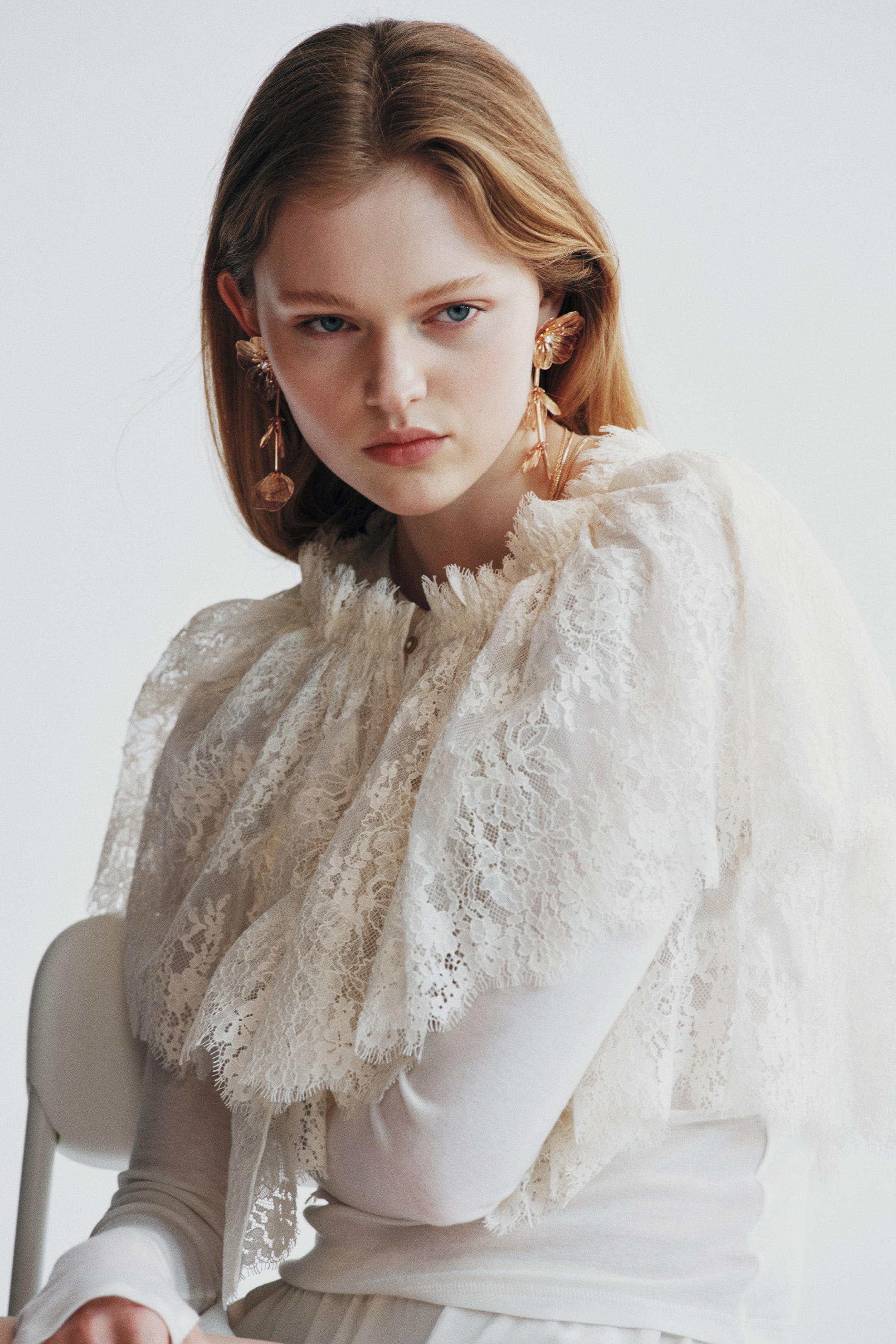 View larger image: The model is wearing flower-shaped metal earrings featuring a sparkling rhinestone at the center, with delicate, translucent, amber-toned petal-shaped pendants dangling from each ear.
