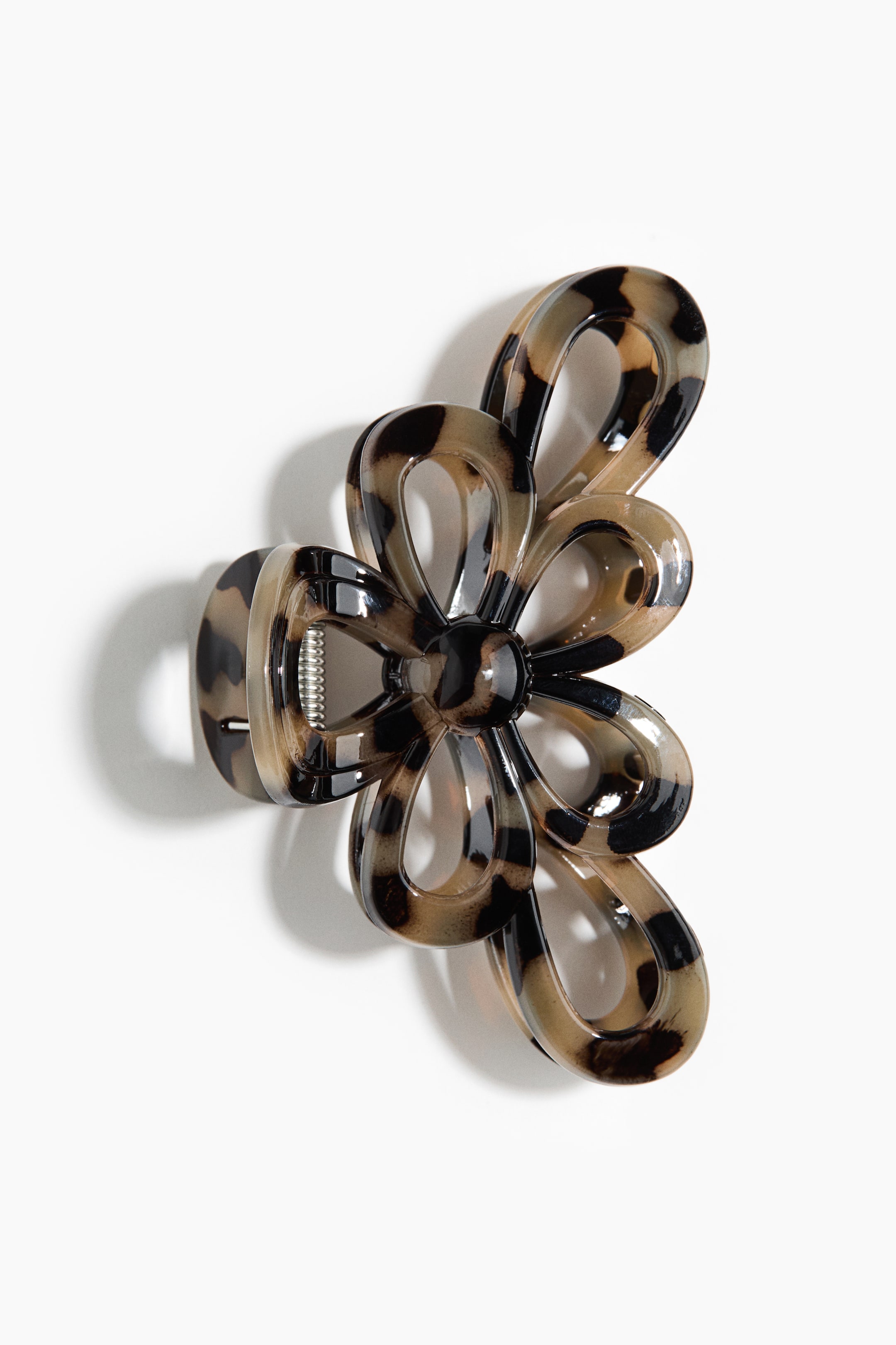 Ampliar la imagen: Un clip de garra para el cabello presenta su parte frontal, con forma de flor con pétalos en forma de bucle y estampado con un diseño traslúcido de carey en tonos de marrón, negro y beige. El mecanismo de resorte metálico es visible dentro de la garra.