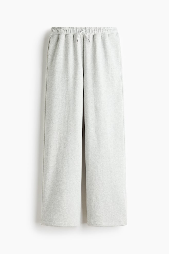 Un par de pantalones de chÃ¡ndal jaspeados en gris claro aparece de frente, con una silueta de pernera ancha y un corte relajado. Los pantalones muestran una cintura elÃ¡stica fruncida con un cordÃ³n ajustable blanco y discretos bolsillos laterales. - 1