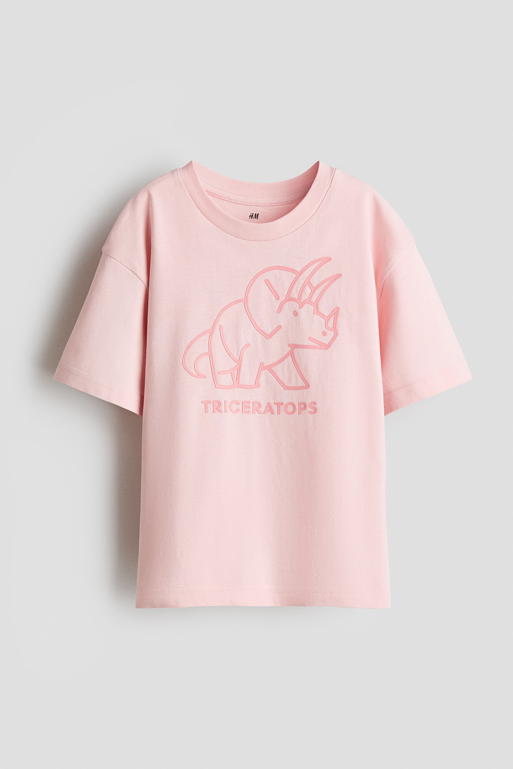 Agrandir l'image: Un t-shirt rose présente son devant, avec un col rond côtelé et des manches courtes. Une illustration en ligne de couleur rose plus foncée d'un Triceratops est affichée au centre de la poitrine, avec le mot 'TRICERATOPS' imprimé directement en dessous.