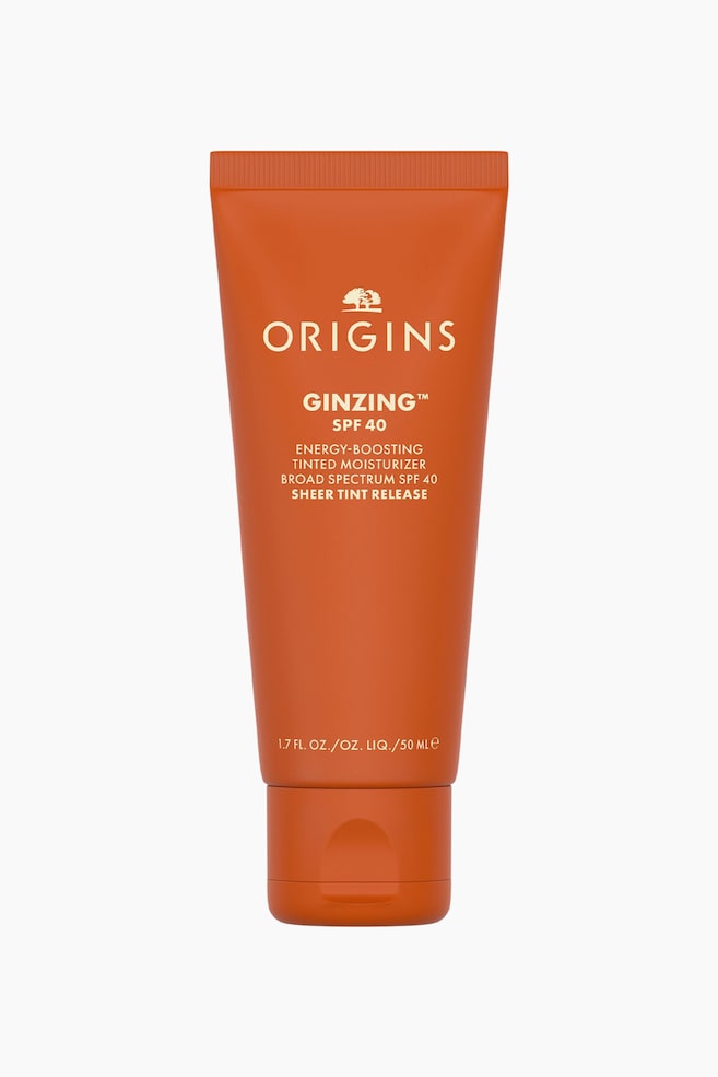 En oransje klemmetube med Origins GinZing SPF 40 Energy-Boosting Tinted Moisturizer stÃ¥r oppreist og vender mot front, med kremfarget tekst som viser merke- og produktinformasjon. Tuben er utstyrt med en matchende oransje flip-top-kork nederst. - 1