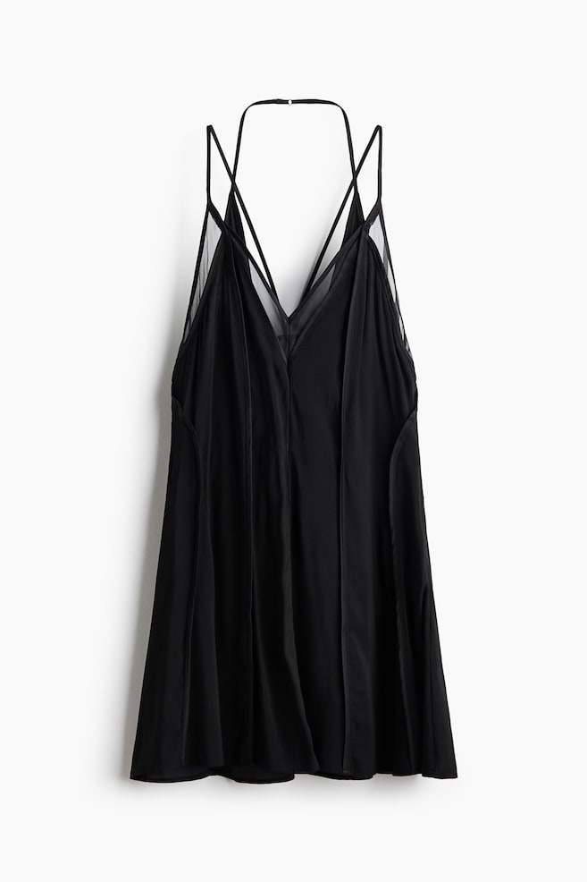 A black sleeveless mini dress is facing front, displaying a deep V-neckline with sheer mesh inserts and a multi-strap halter design. The garment is hanging flat, showcasing its fluid silhouette and subtle vertical panel seams. - 1