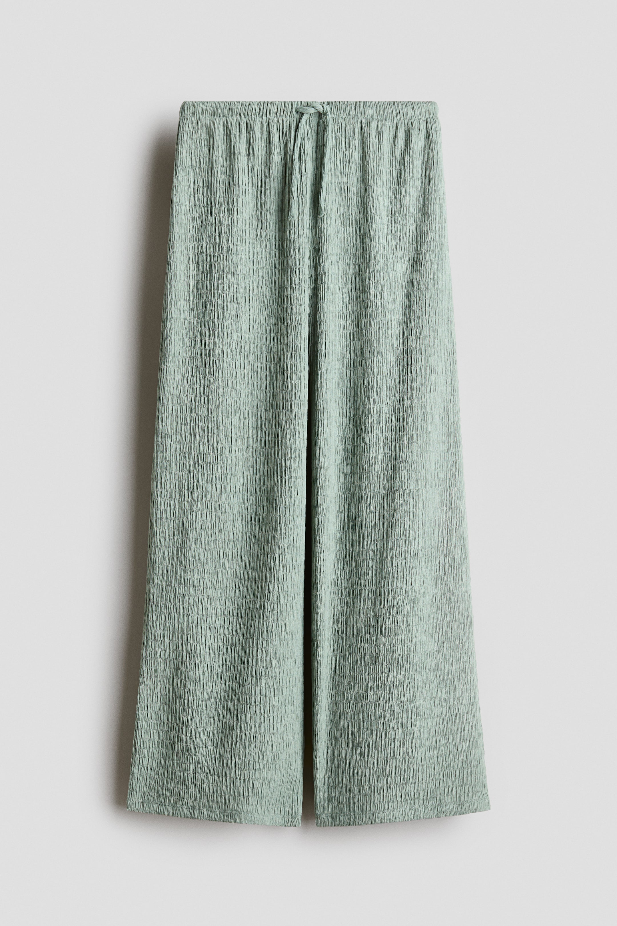 Ampliar la imagen: Los pantalones verde claro se presentan en vista frontal, mostrando una tela de jersey texturizada, una cintura elástica con un cordón visible atado en el centro y piernas rectas.
