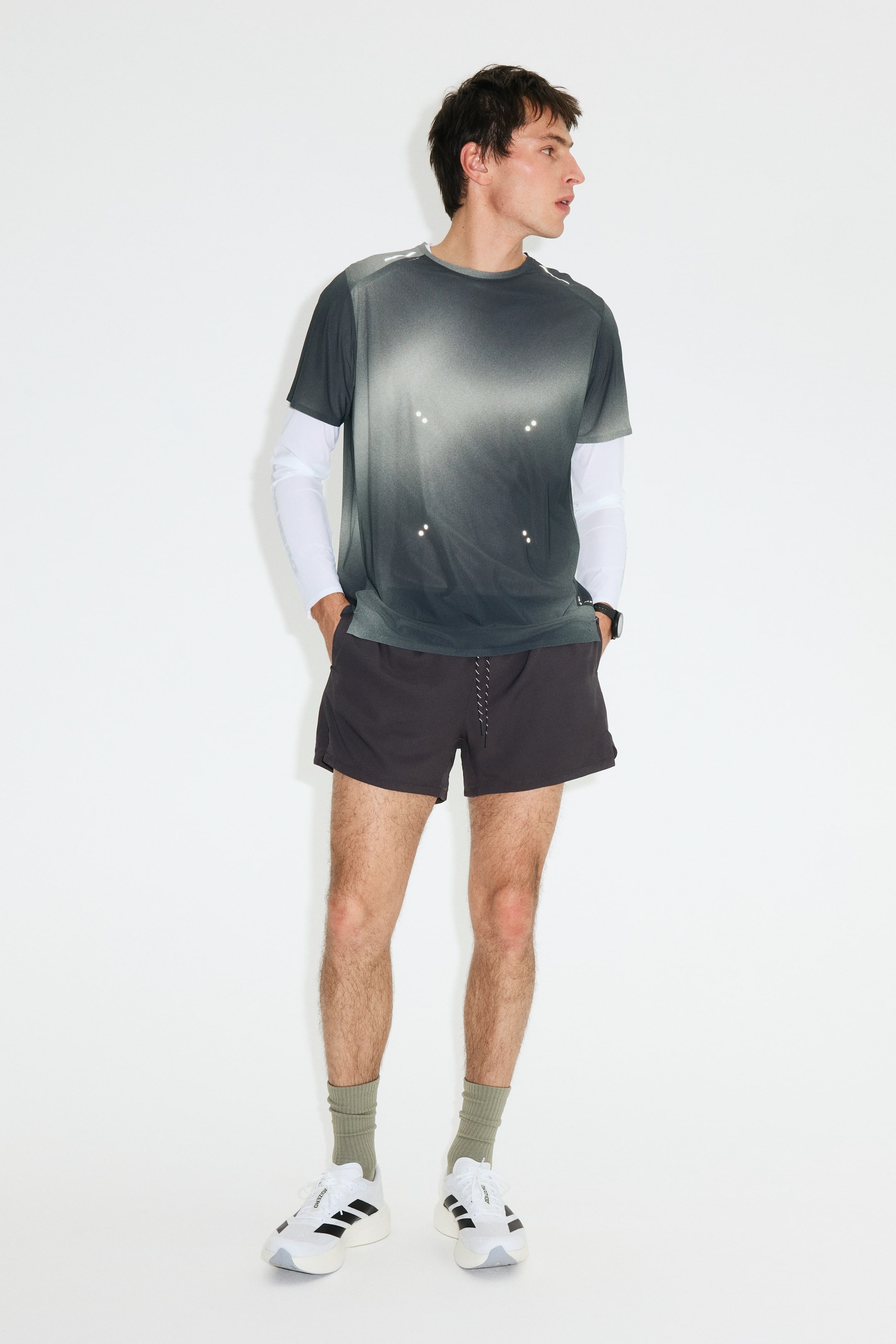 Agrandir l'image: Un t-shirt à manches courtes et col rond présente un dégradé de gris à noir avec des points réfléchissants dispersés sur le devant, porté par-dessus une chemise à manches longues blanche.
