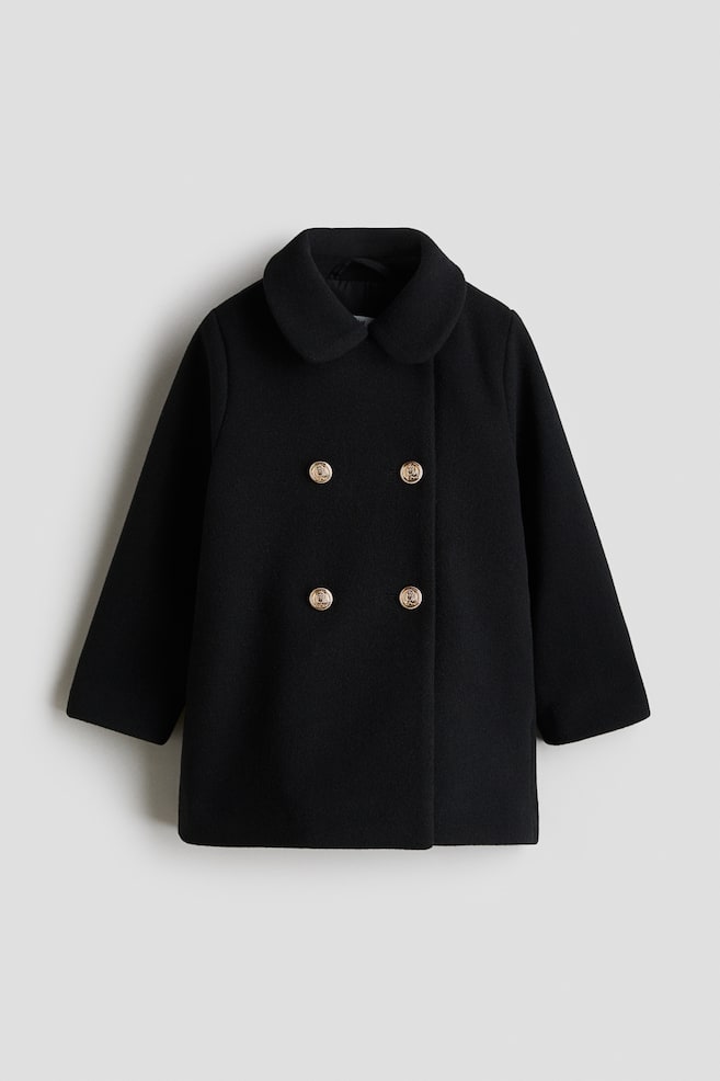 Een zwarte dubbelrijige jas toont zijn VOORKANT, met een gevilte weefsel en een afgeronde kraag. Het is ontworpen met verlaagde schouders en toont vier goudkleurige knopen die in twee kolommen aan de voorkant zijn gerangschikt. - 1