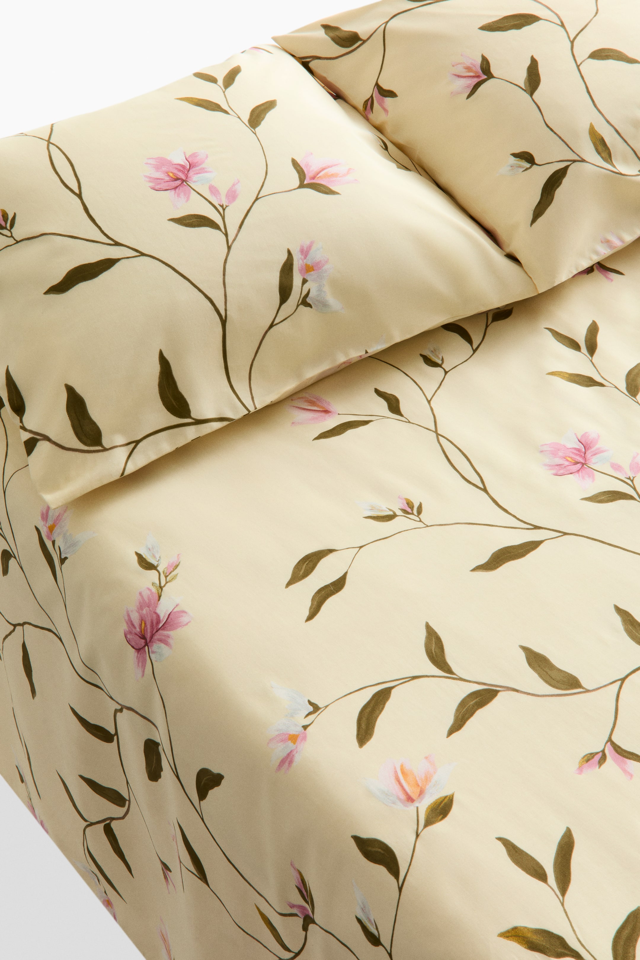 View larger image: A king-size bedsheet set in a patterned cotton weave features a floral design. A flat sheet and a pillow cover are visible, both bearing delicate brown-green vines with scattered pink and white flowers on a light-yellow fabric.