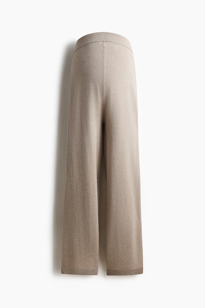 Beige Strickhosen werden von hinten präsentiert und zeigen eine hohe, gerippte Taille sowie lange, weite Beine mit Rippungen an den Säumen. - 1