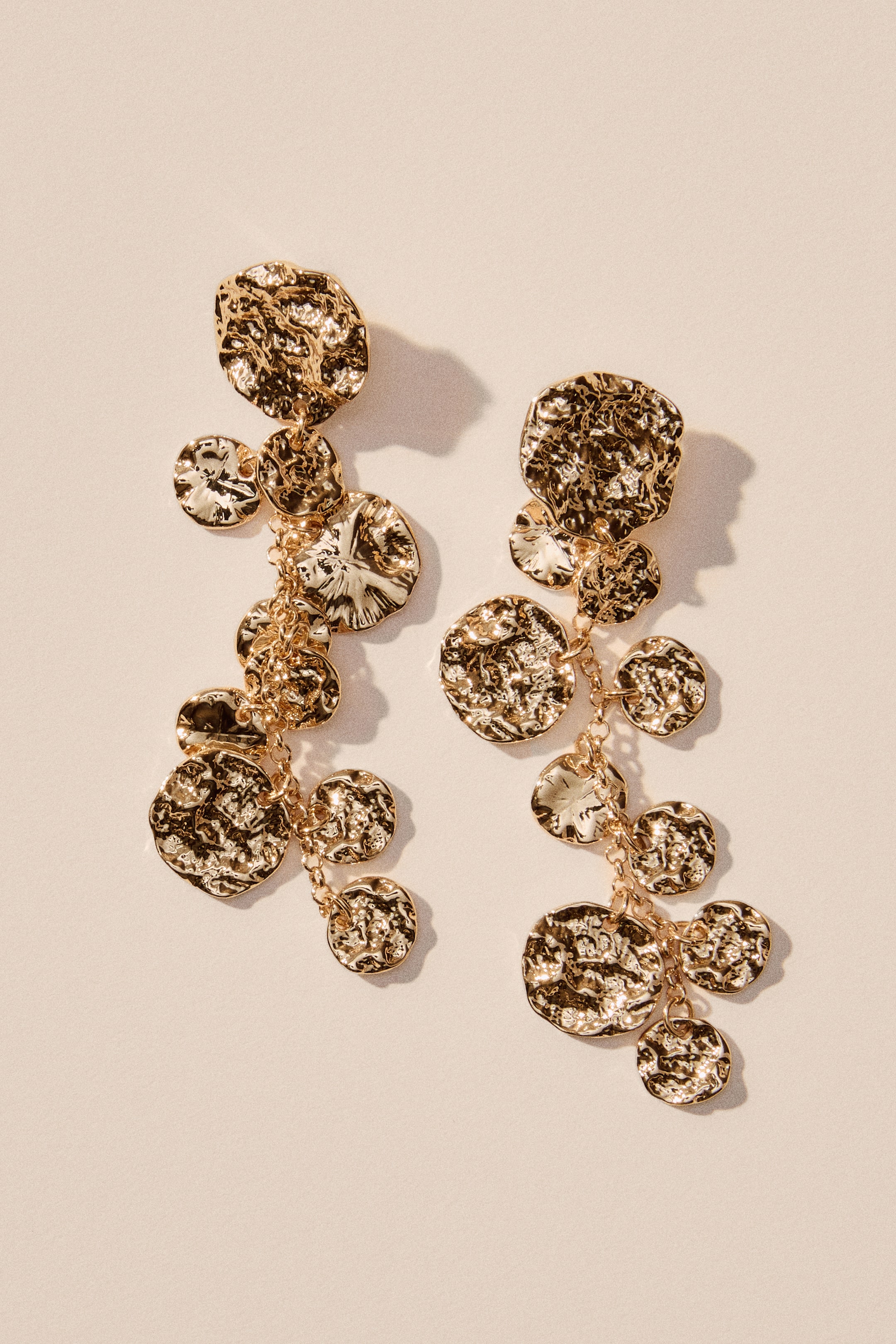 View larger image: A pair of gold-toned dangle earrings featuring multiple irregularly shaped, hammered metal pieces. These pieces are interconnected by small chains, creating a cascading arrangement.