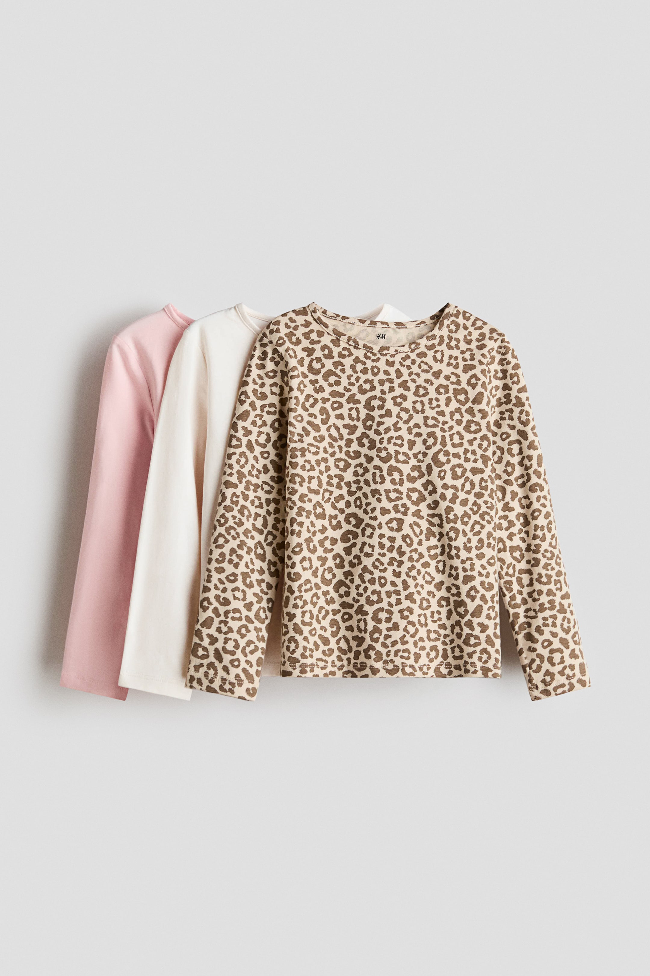 View larger image: Three long-sleeved tops are arranged in a stack, facing forward and slightly to the right. The topmost garment showcases a beige background adorned with a brown leopard print. The middle piece is a solid off-white, while the bottom one is a solid light pink. Each top features a round neckline with a narrow trim, reflecting a subtle yet stylish design.