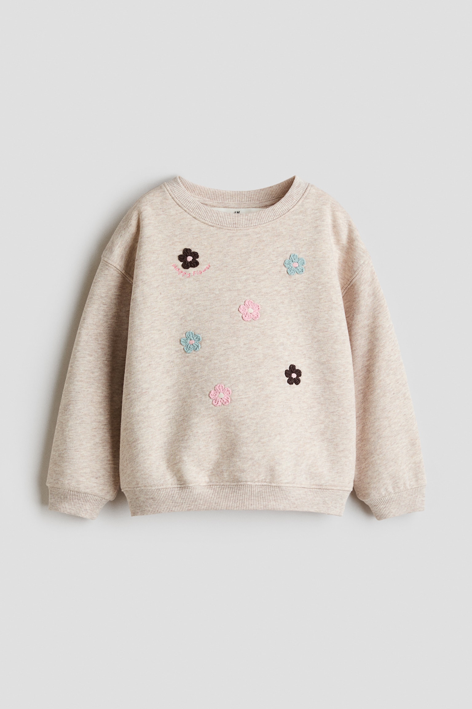 A light beige melange sweatshirt is shown from the front, featuring a round, rib-trimmed neckline, dropped shoulders, and ribbed cuffs and hem. The front showcases scattered small embroidered floral details in pink, light blue, and dark brown.