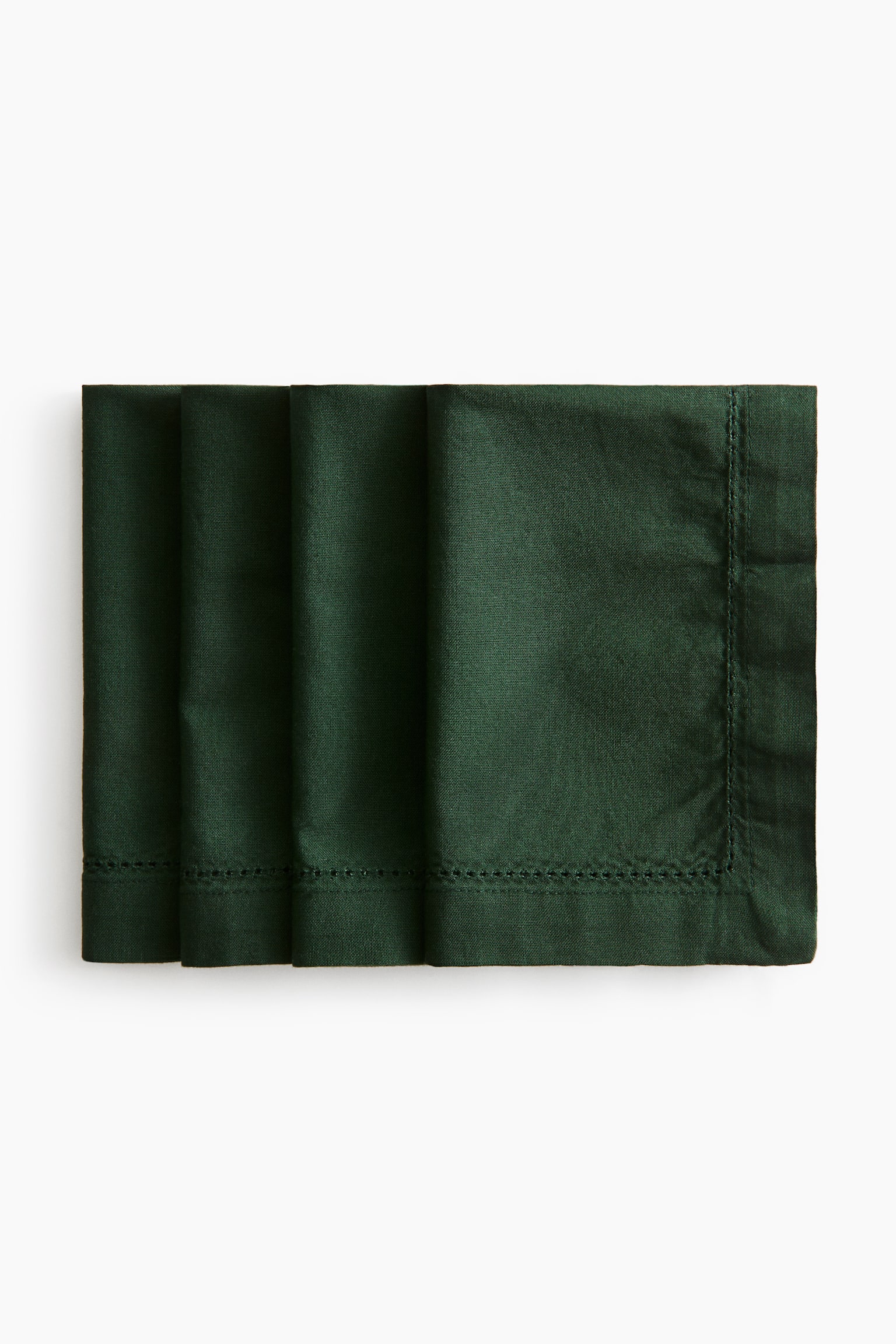 Four dark green cotton canvas napkins are overlapping in a neat horizontal stack, shown from the front. Each napkin is displaying a delicate hemstitching border running parallel to a wide, structured hem.