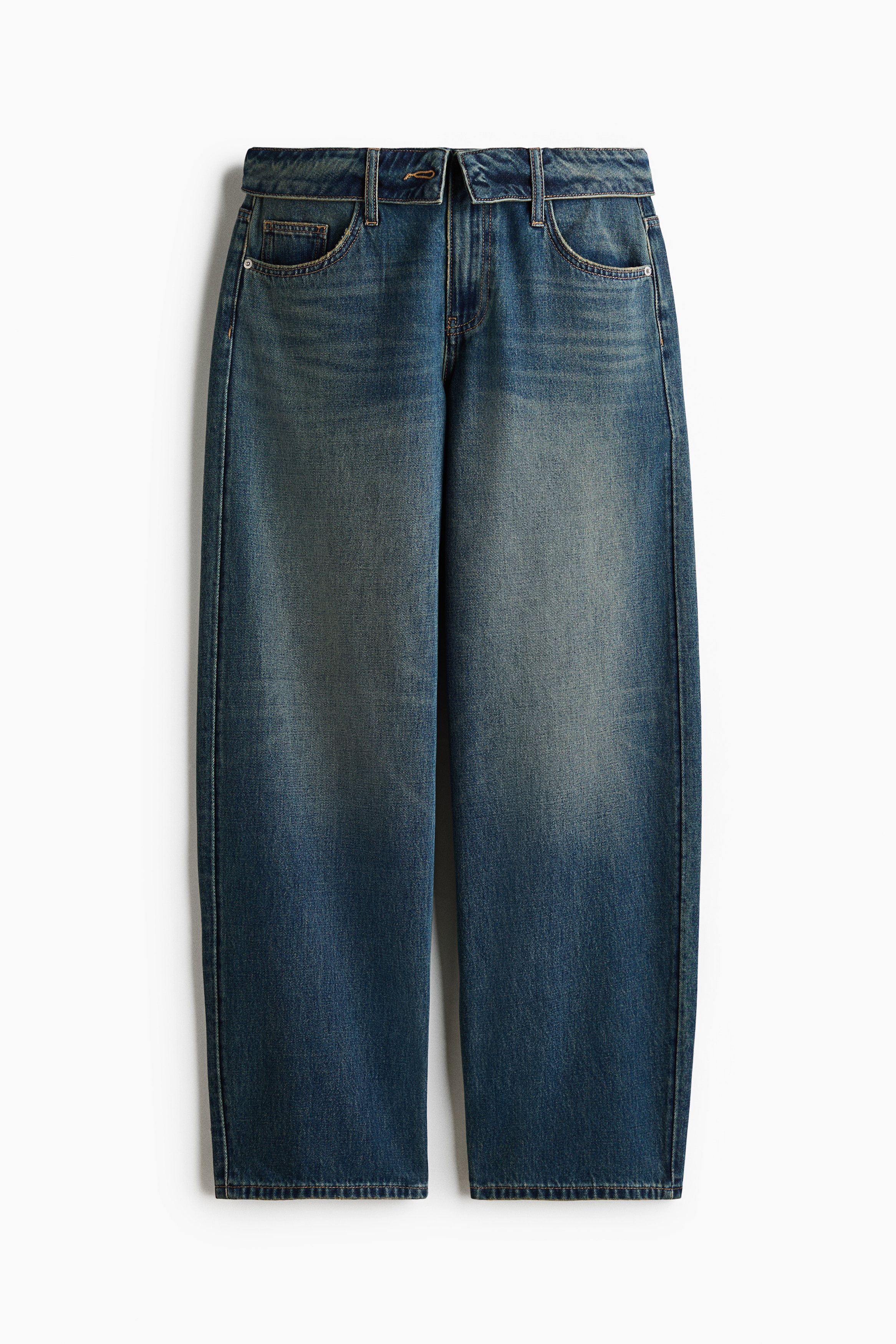 Wide-leg blue jeans with a relaxed fit and faded wash are worn by the model. The jeans are paired with a white halter top, a black leather jacket draped off the shoulders, and white sneakers.