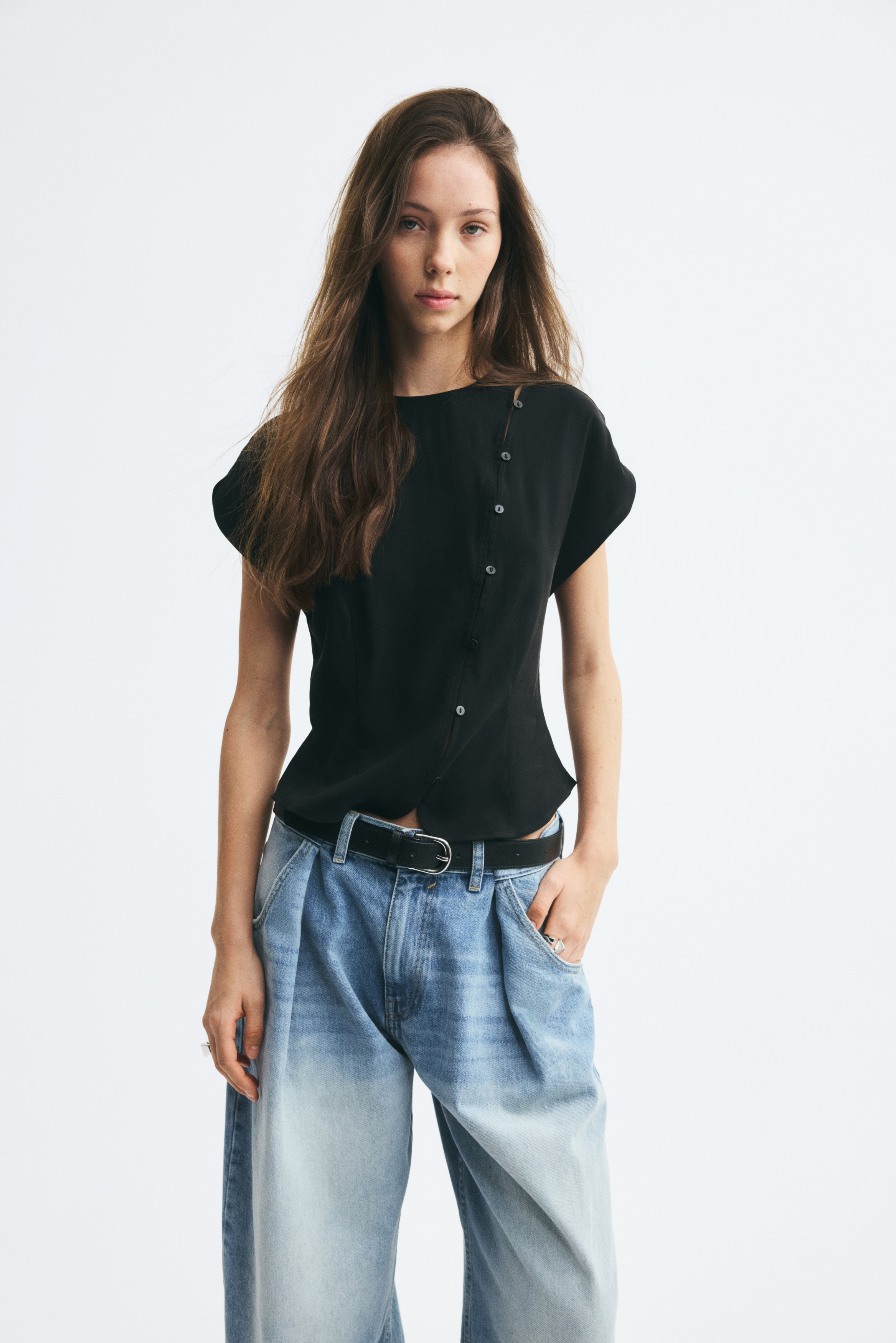 Má»t chiếc áo blouse tay ngắn mà u Äen Äang ÄÆ°á»£c chụp chÃnh diá»n, là m ná»i báºt phần cá» tròn và tay áo cánh tiên rá»§. Thiết kế có hà ng cà i nút chéo bất Äá»i xứng vá»i các nút trắng và Äen tương phản, chạy từ vai trái xuá»ng Äến gấu áo cong xẻ tà .