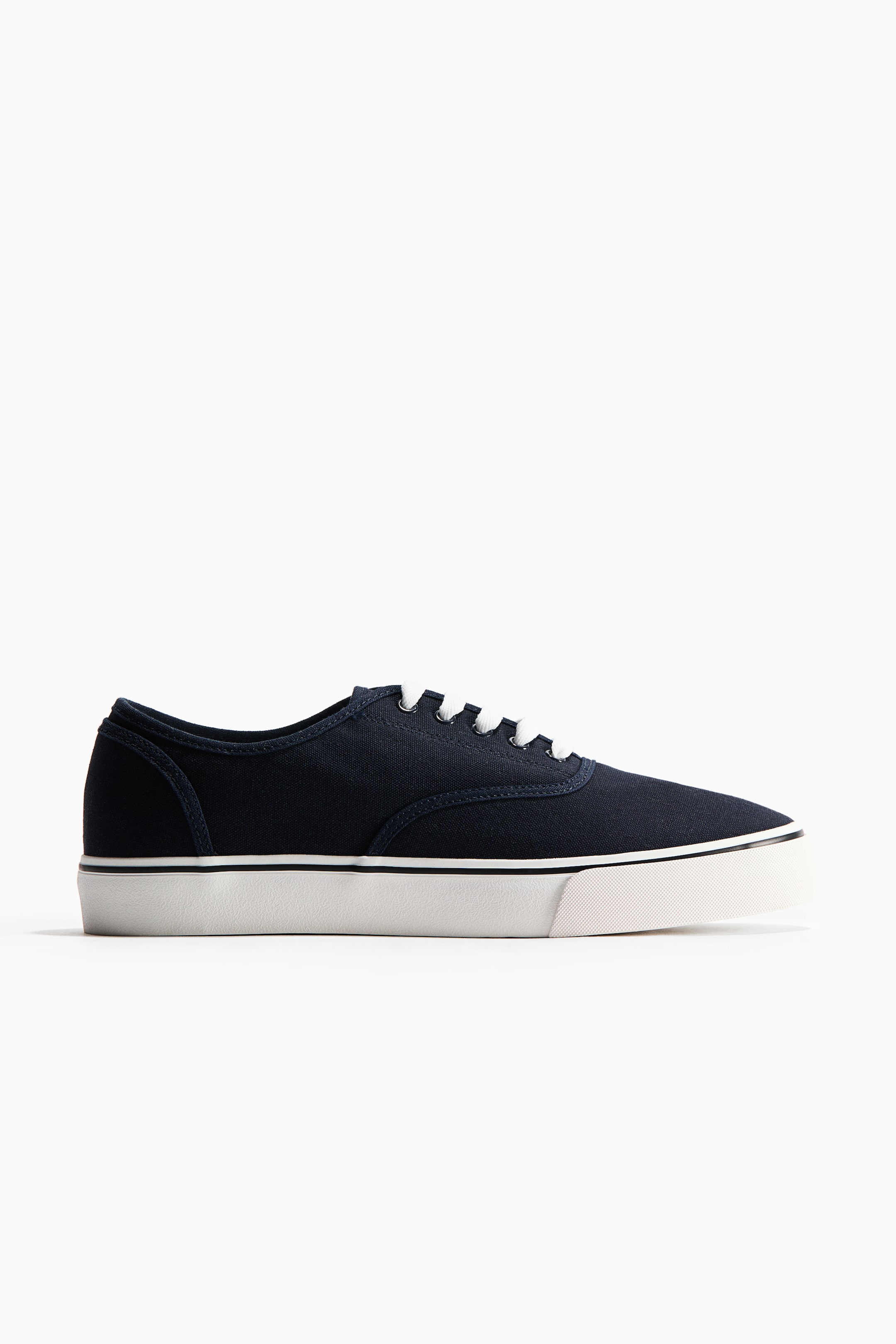 View larger image: Trainers showcase a navy cotton canvas upper and white lacing at the front, complemented by a white rubber sole with a thin black stripe along its top edge.