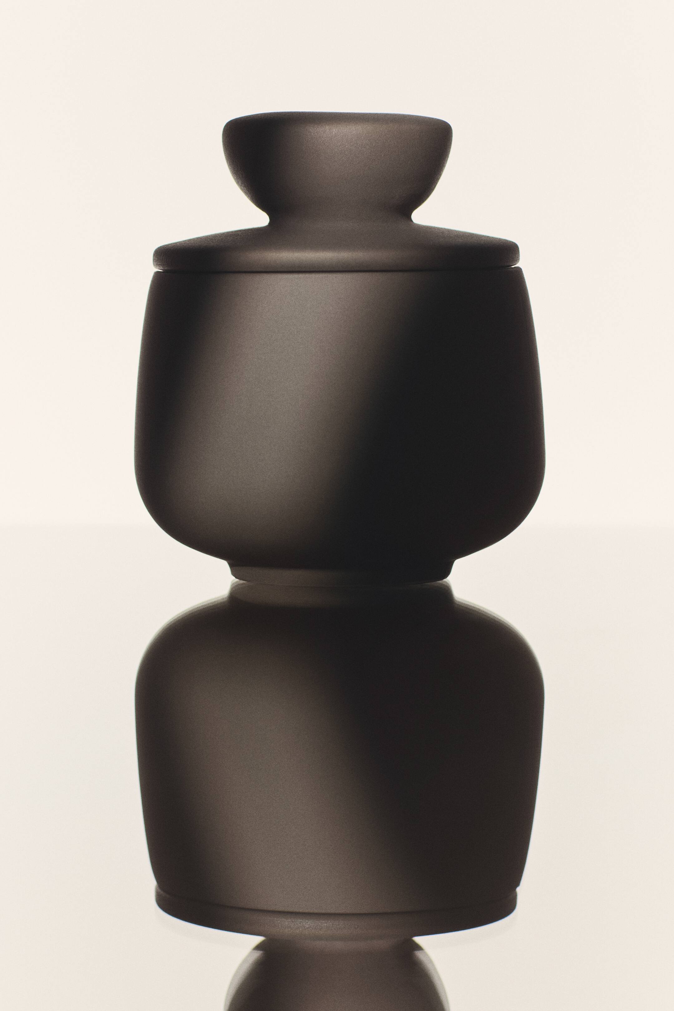 View larger image: A dark brown matt stoneware pot with a rounded body and a lidded top featuring a flared knob is standing on a reflective surface, displaying a clear, symmetrical reflection below it from a front-facing angle.