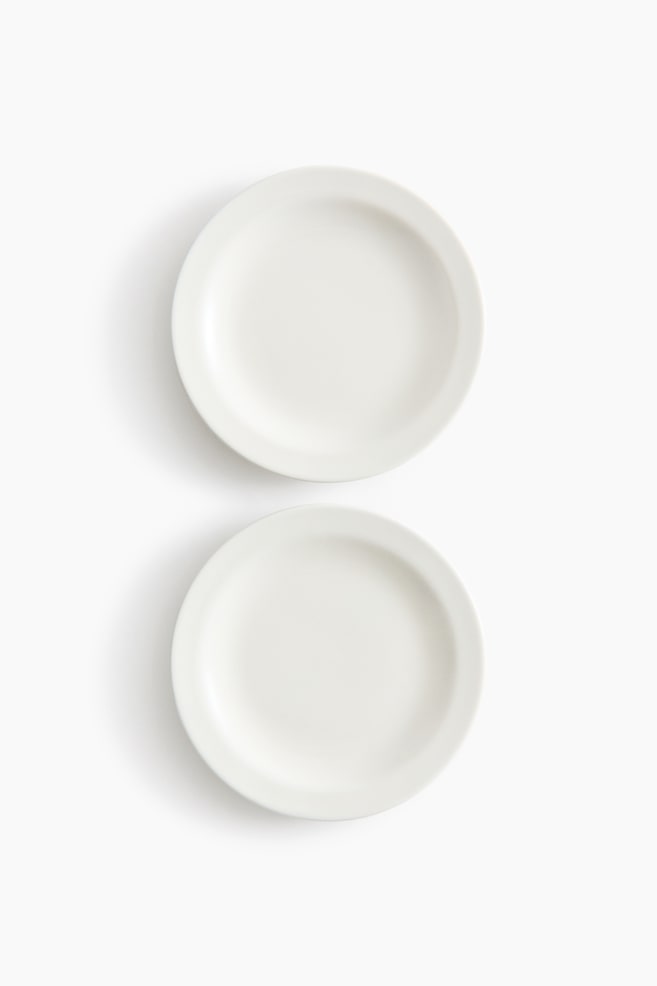 Duas placas redondas brancas idênticas estão deitadas planas e viradas para cima, cada uma com uma borda ligeiramente elevada, posicionadas verticalmente uma acima da outra. - 1