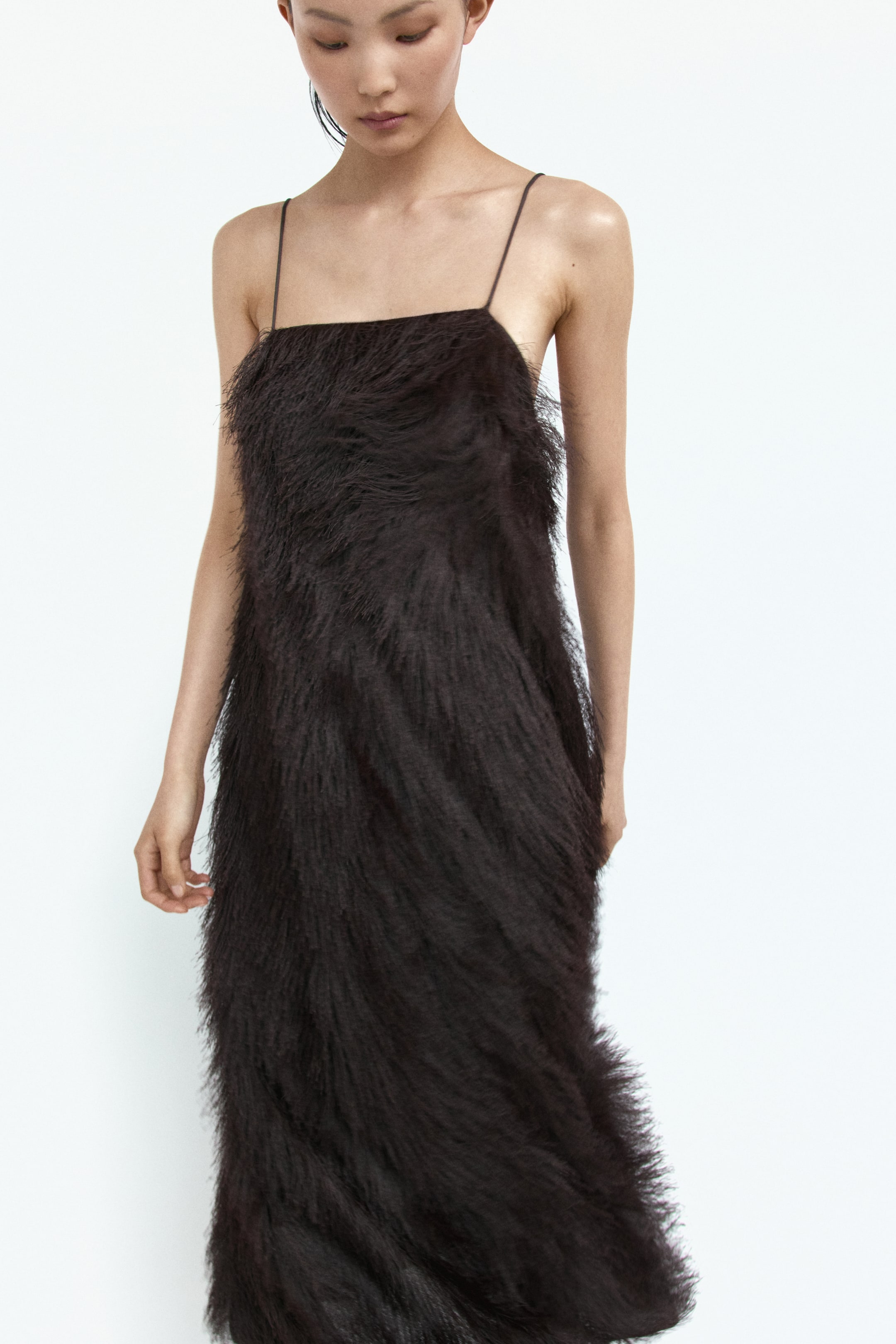 Grotere afbeelding bekijken: Een donkerbruine jurk toont een ruige, langharige textuur van boven naar beneden. Het heeft een rechte, midi-lengte silhouet met een vierkante halslijn en dunne spaghettibandjes, iets naar rechts gericht.