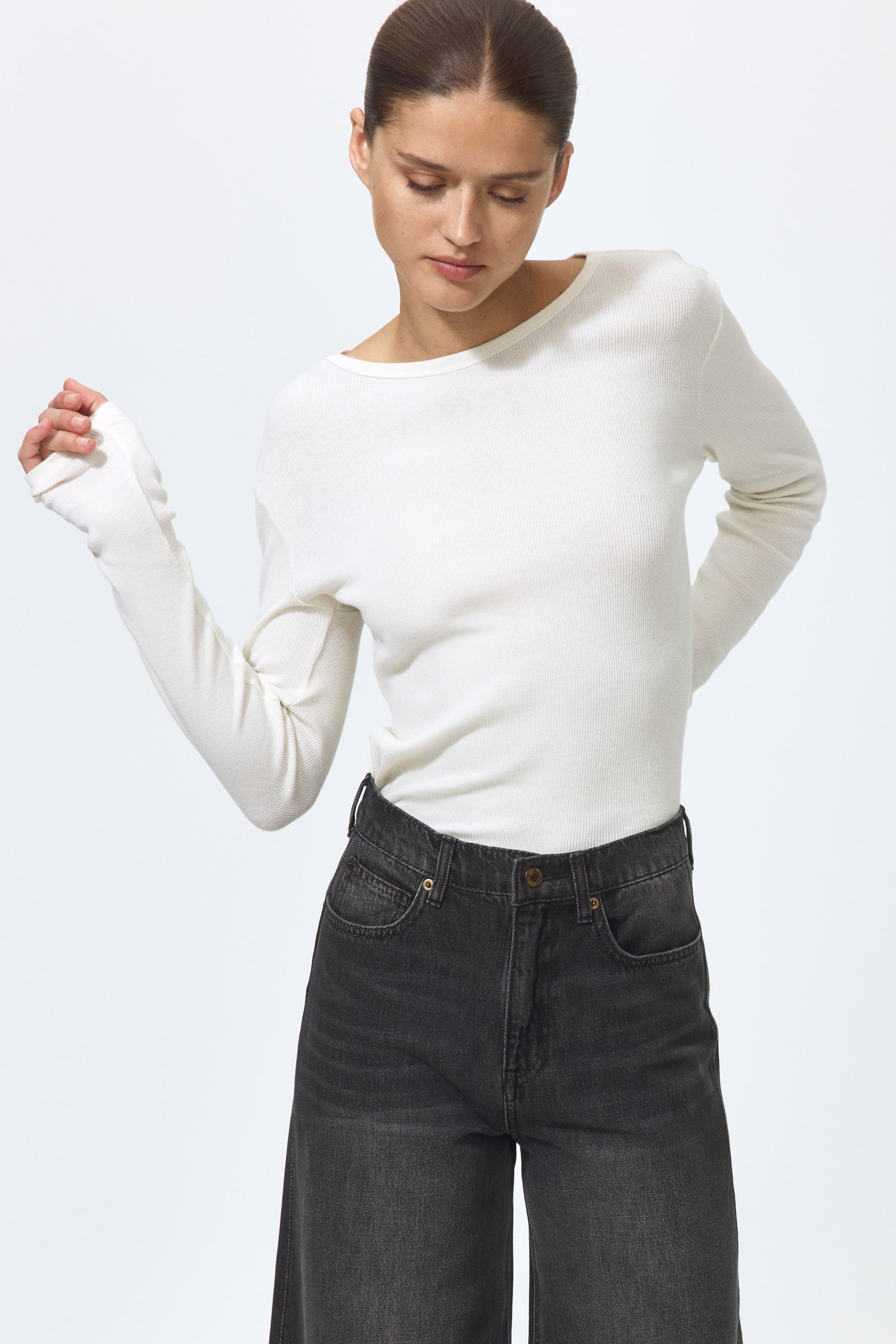 Visualizza immagine più grande: Jeans a 5 tasche grigio scuro con vita alta, gamba ampia e zip frontale visibile con chiusura a bottone, indossati dalla modella con un top bianco a maniche lunghe infilato nella cintura.