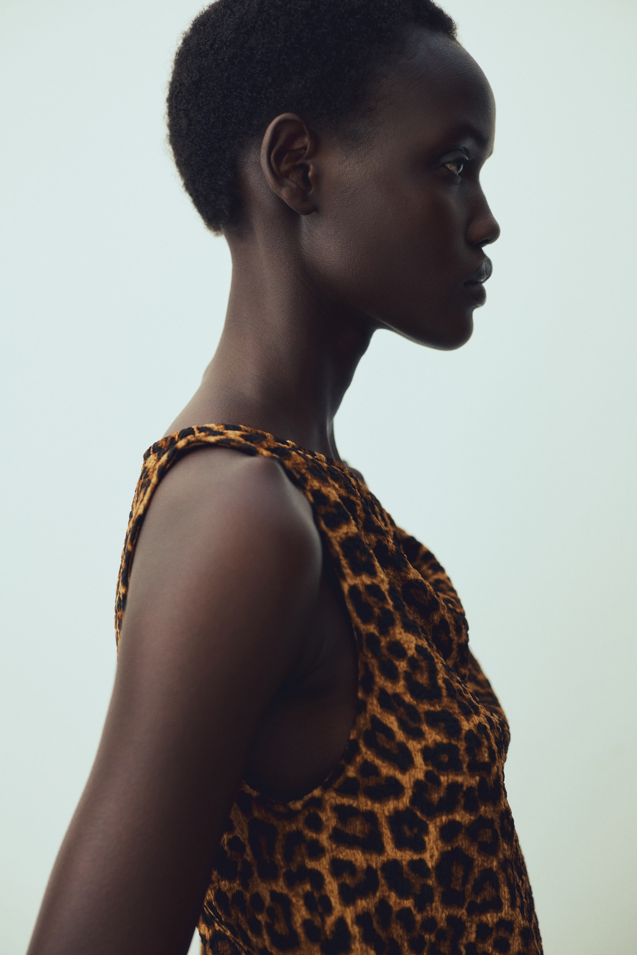 Ampliar la imagen: "Una blusa sin mangas de estampado de leopardo, con manchas negras sobre un fondo marrón cálido, presenta un escote suavemente drapeado mientras se muestra de perfil izquierdo."