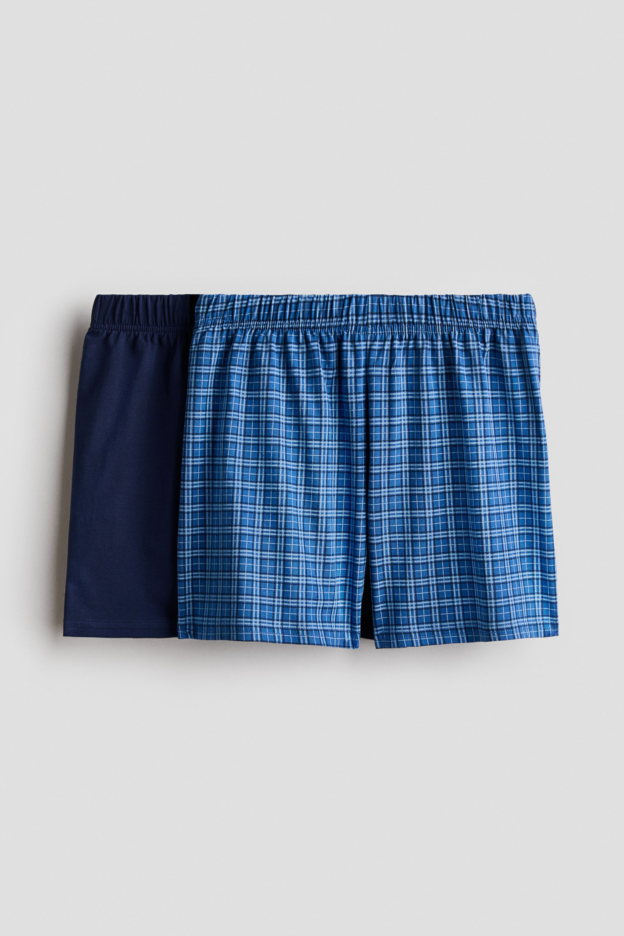 Agrandir l'image: Deux paires de shorts de pyjama sont présentées de face, toutes deux dotées d'une taille élastiquée. Une paire est de couleur bleu marine uni, tandis que l'autre arbore un motif à carreaux bleus.