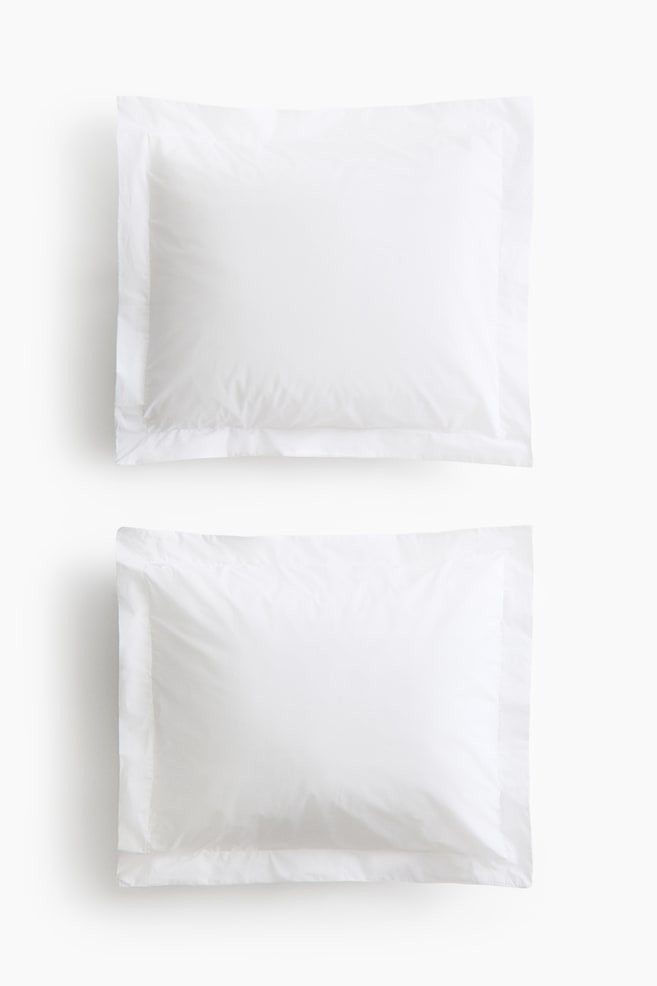 Two white cotton percale pillowcases are facing forward, arranged vertically to display their smooth, matte finish. Each pillowcase features a wide, flat flange border along all four edges. - 1