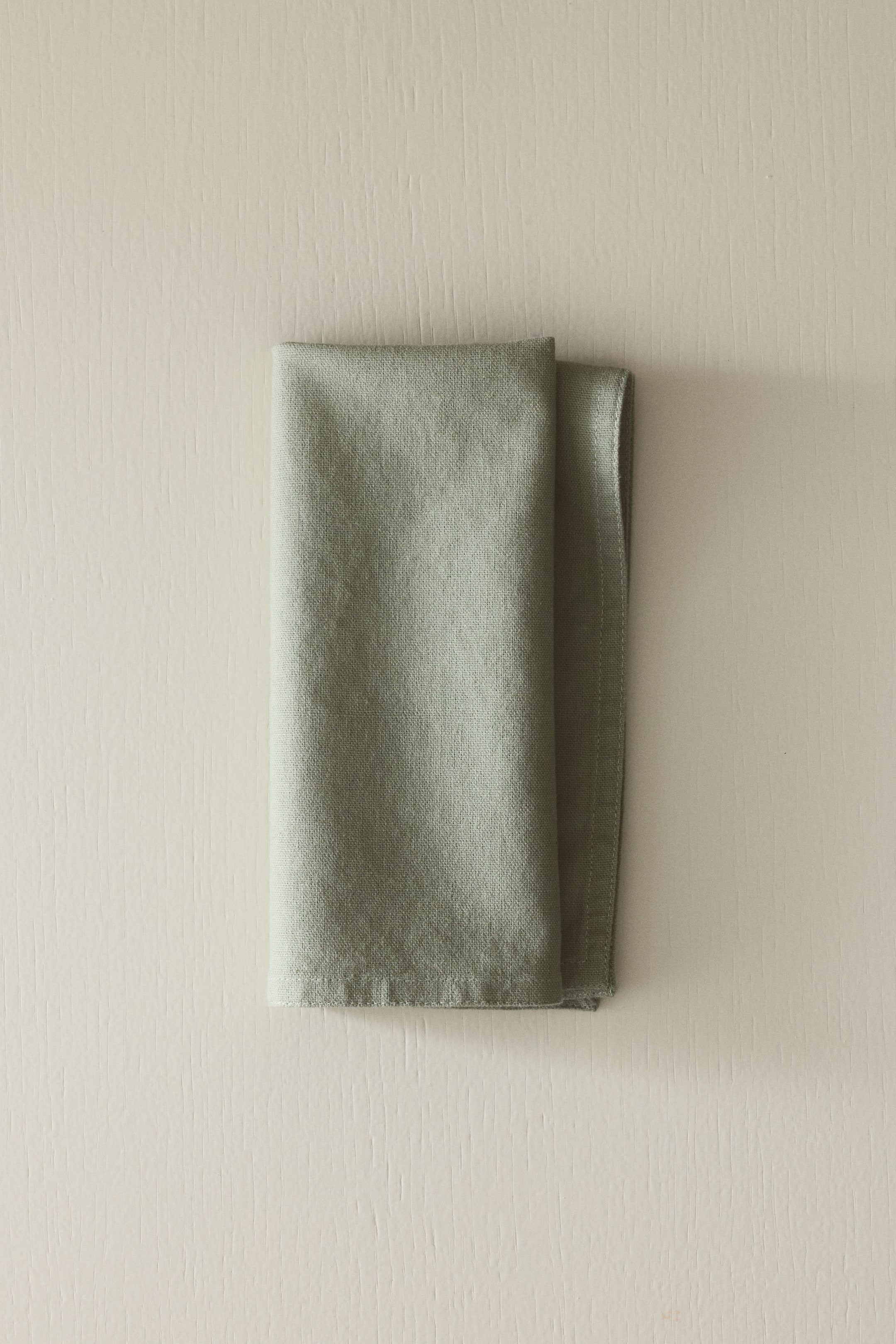 View larger image: A napkin is folded, displaying a muted green color and a visible, slightly textured weave.