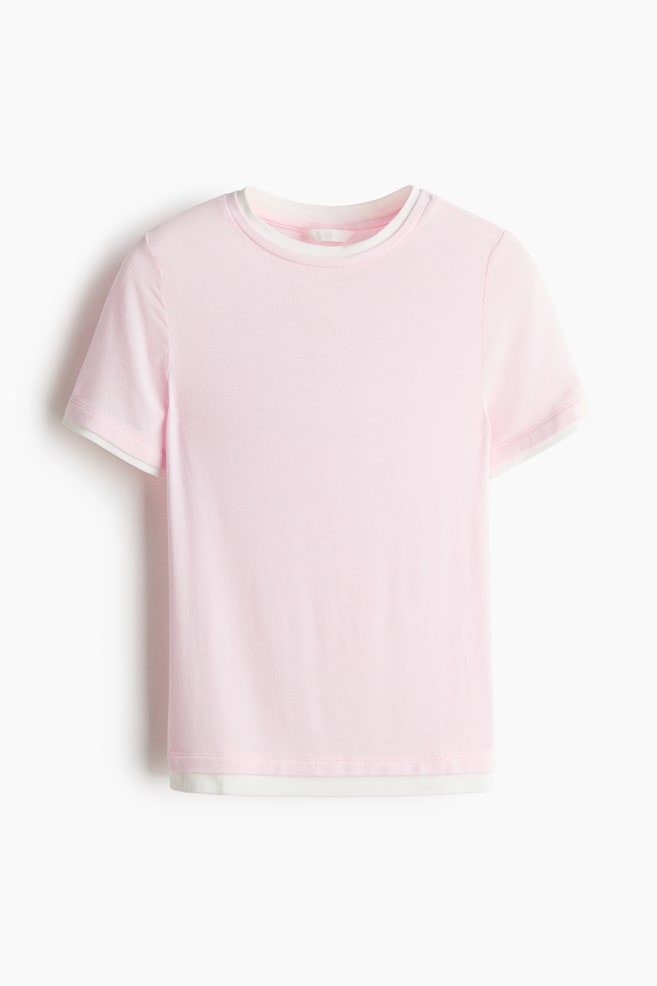 The pink t-shirt is presenting a layered design, with white fabric visibly extending from the crew neck, short sleeve cuffs, and straight hem. - 1