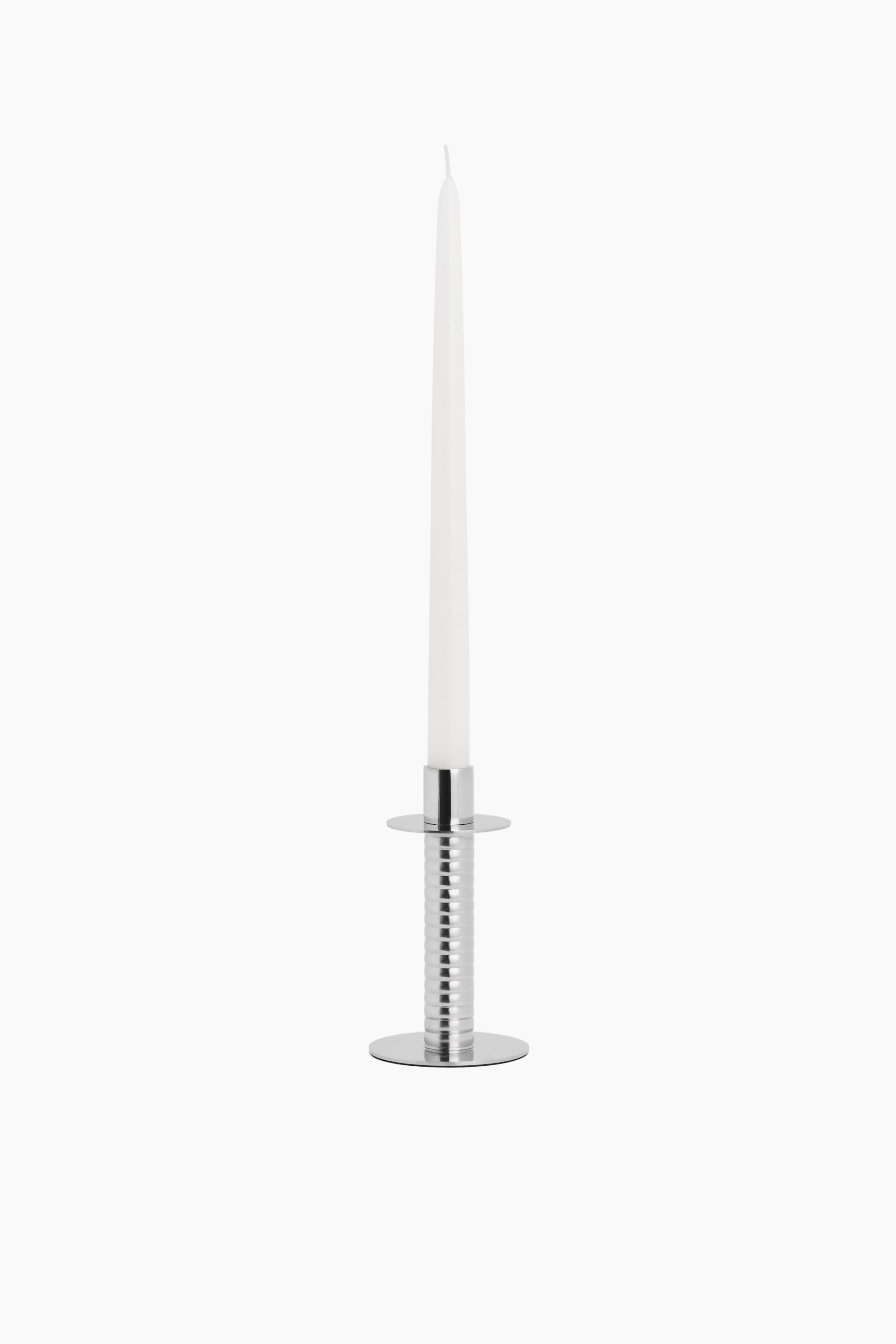 View larger image: A polished stainless steel candlestick showcases a circular base and a ribbed cylindrical body, with a slender white candle elegantly poised in its top holder.