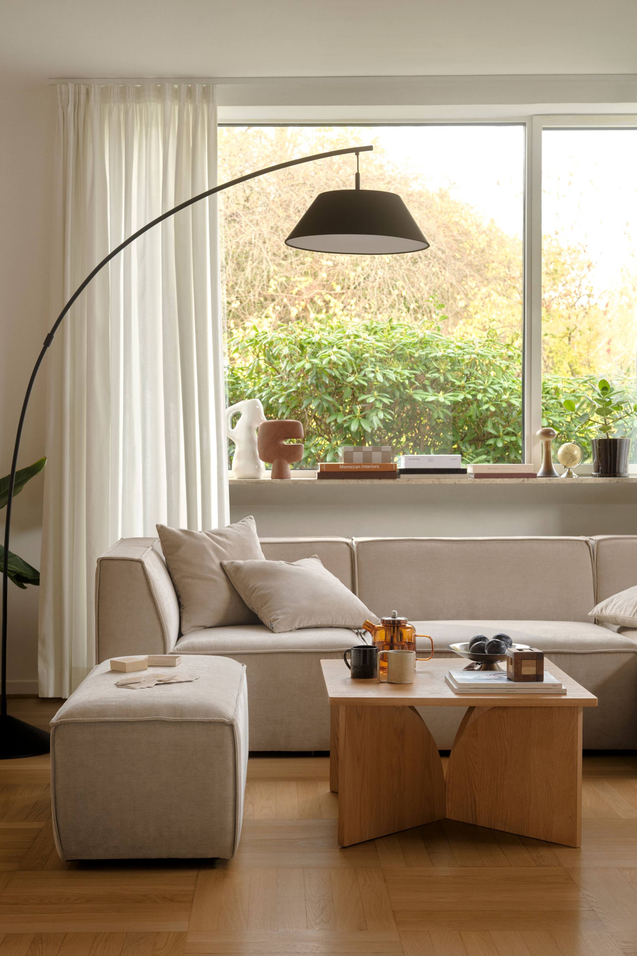 Agrandir l'image: Une table basse rectangulaire en chêne clair met en valeur un design minimaliste avec un plateau plat soutenu par un piétement sculptural composé de quatre panneaux en bois incurvés vers l’intérieur. La table présente à sa surface une théière en verre, des mugs en céramique et une petite boîte en bois.