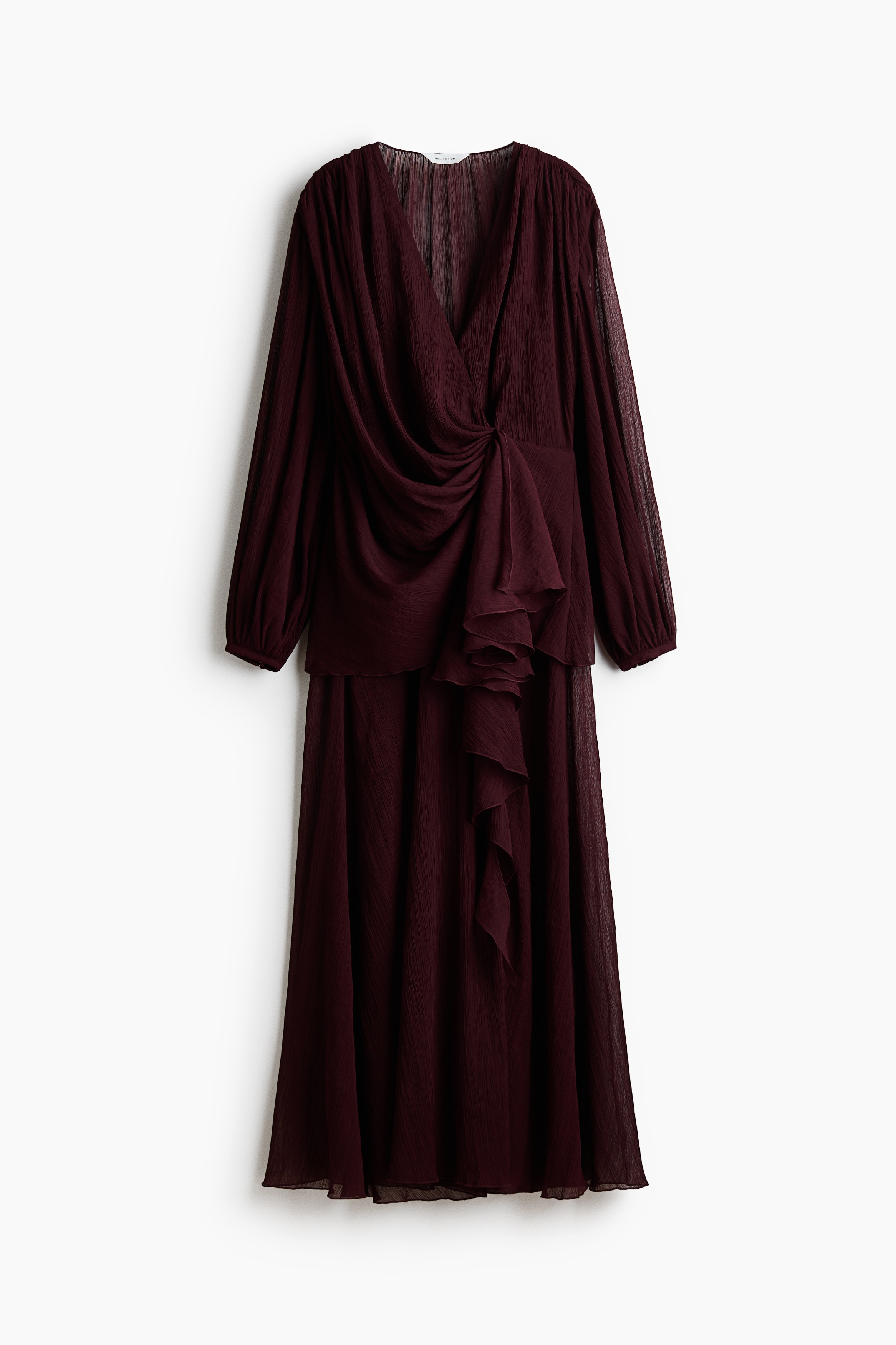 Une robe longue bordeaux foncÃ© en tissu transparent et froissÃ© est portÃ©e par le mannequin, avec un profond dÃ©colletÃ© en V, un devant croisÃ© drapÃ© agrÃ©mentÃ© dâun dÃ©tail torsadÃ©, de longues manches ballon et une fente haute sur le devant. La robe est associÃ©e Ã  des bottes noires montantes visibles Ã  travers la fente.
